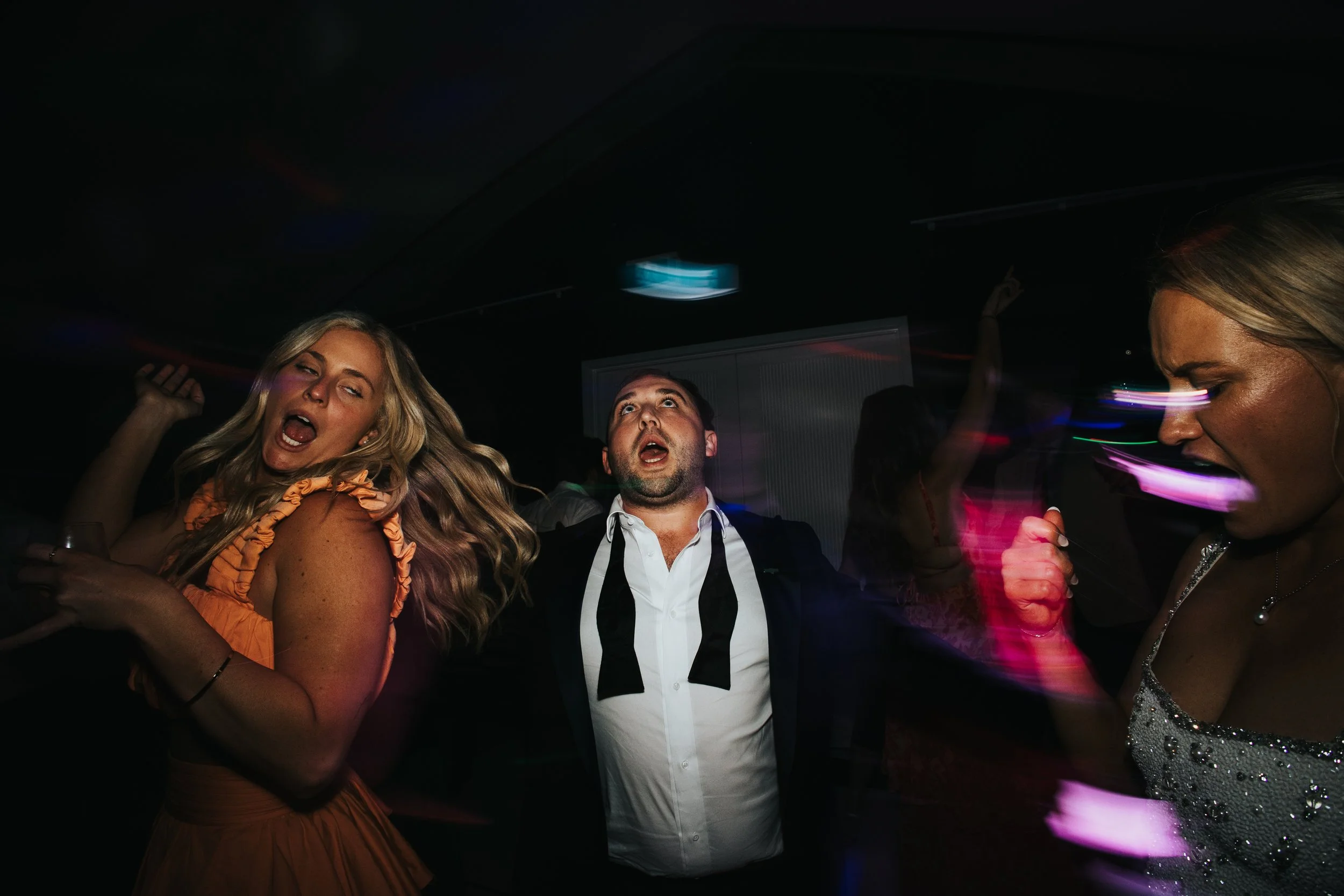People dancing and enjoying themselves at a party in a dark room with colorful lights.