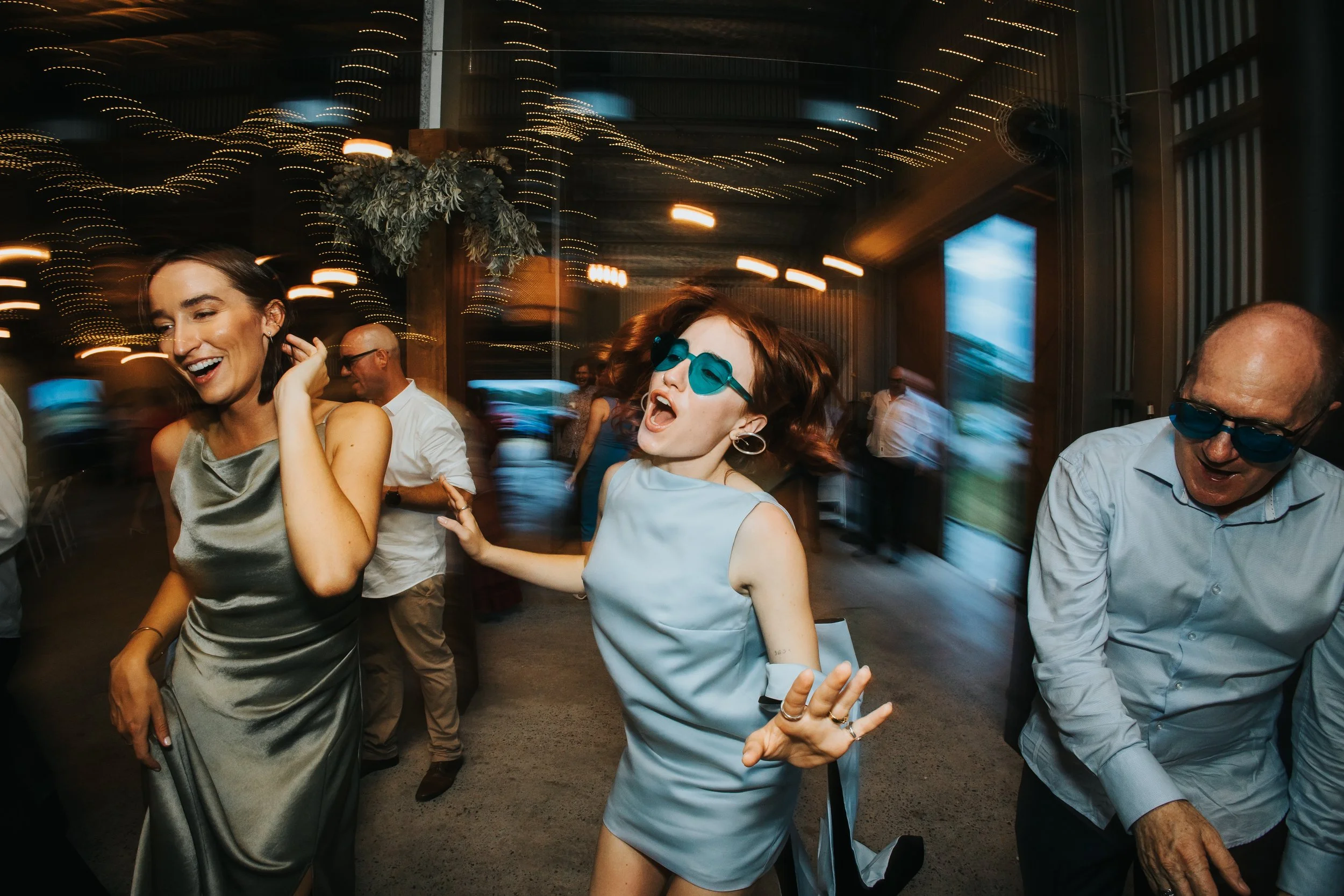 People dancing and enjoying themselves at a party or celebration, with colorful lighting and decorations in the background.