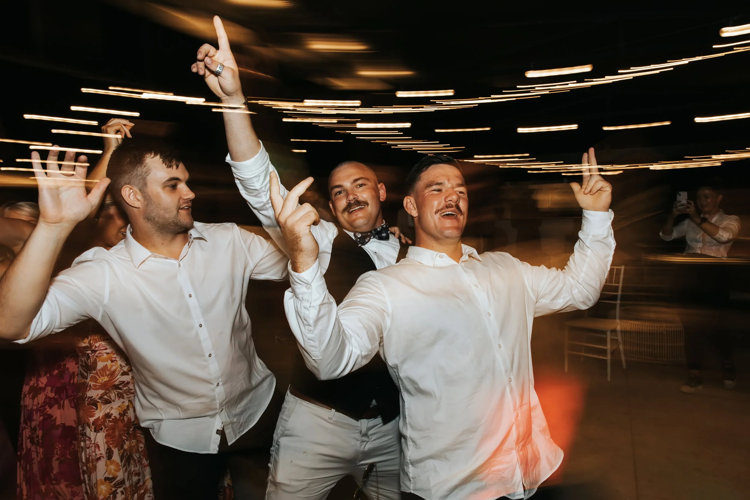 Group of men dancing at a party with blurred lights in the background.