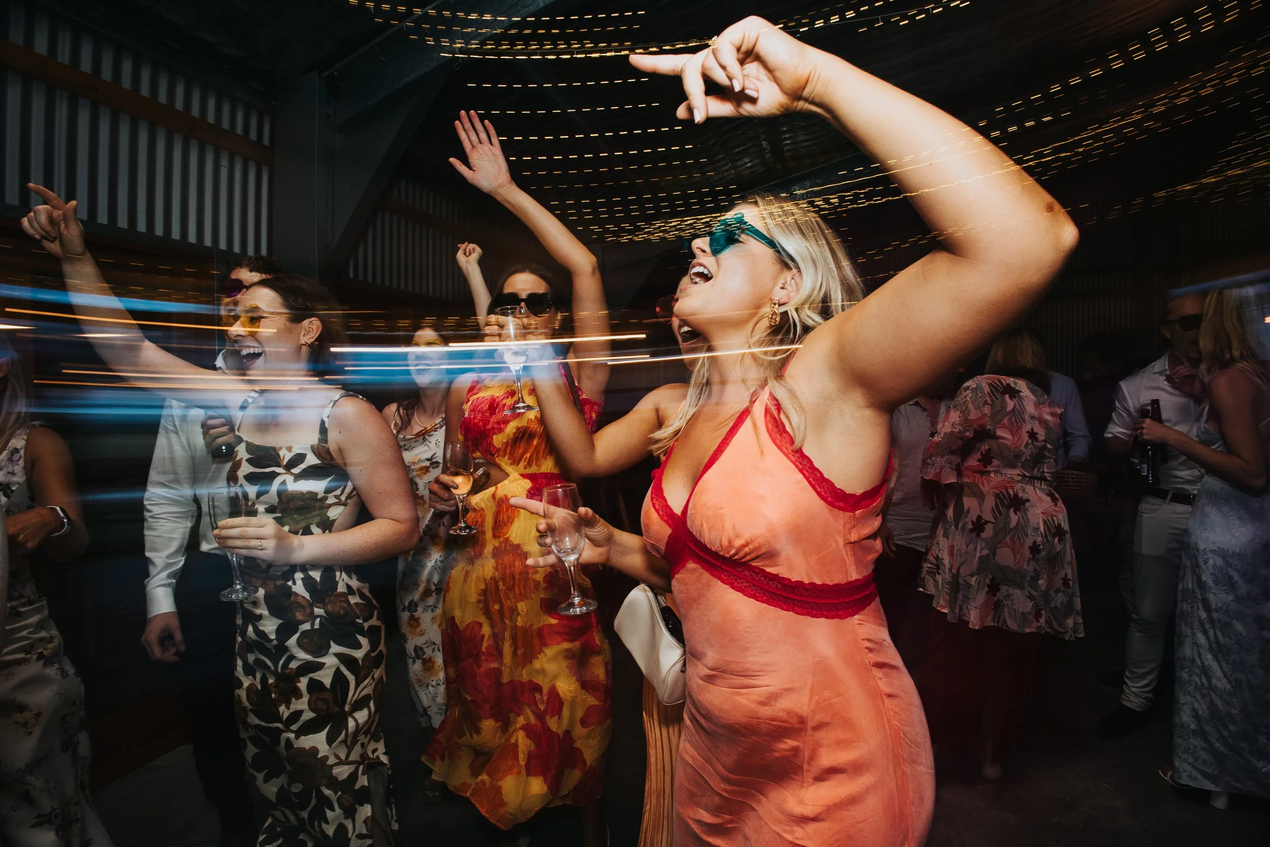 Group of women dancing and celebrating at a party with colorful lights and drinks.