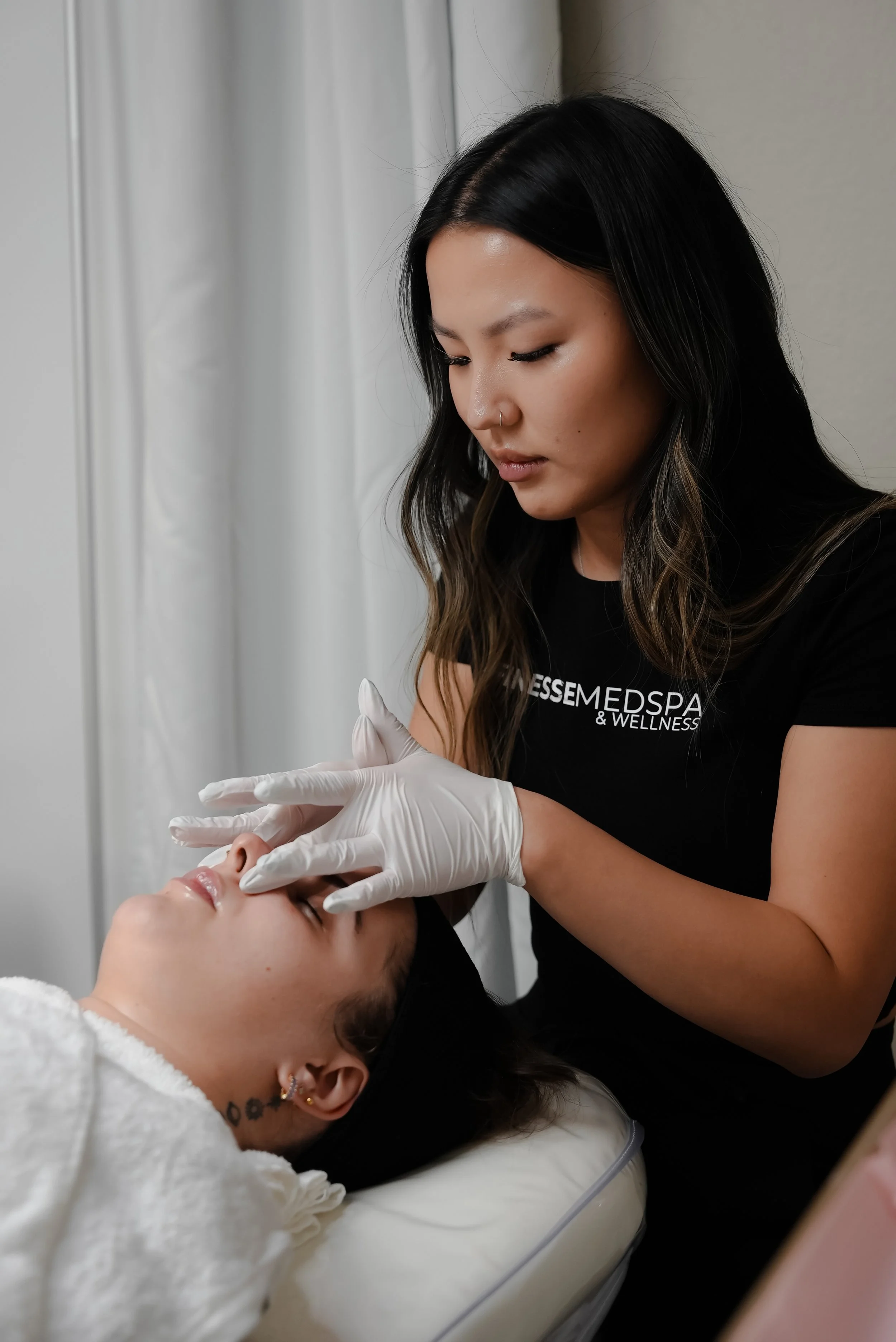A woman receiving a facial treatment from a skincare professional at a wellness spa, with the professional wearing white gloves and focused on the patient's face.