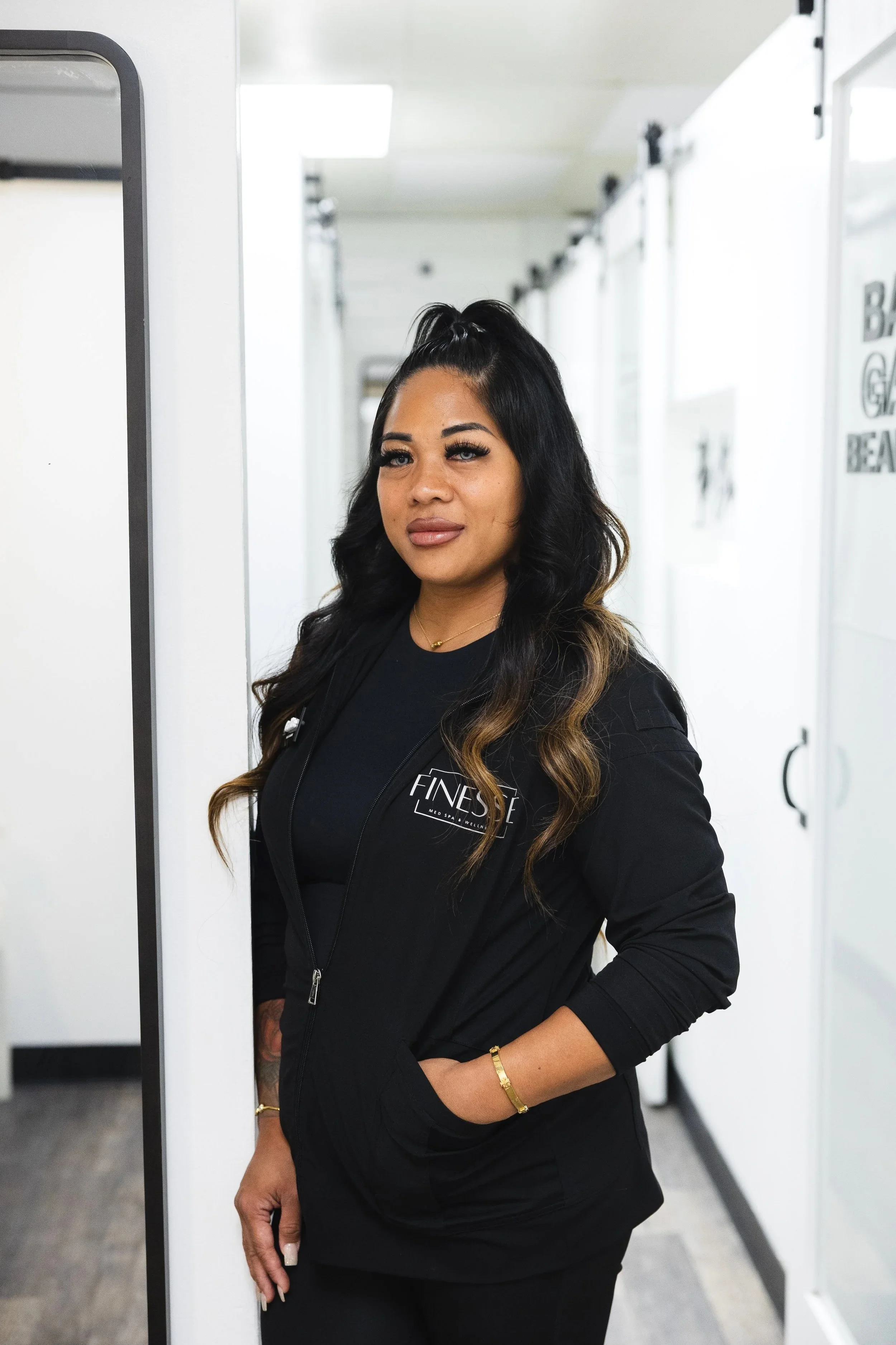 A woman with long wavy hair wearing a black jacket and black shirt standing in a locker room.