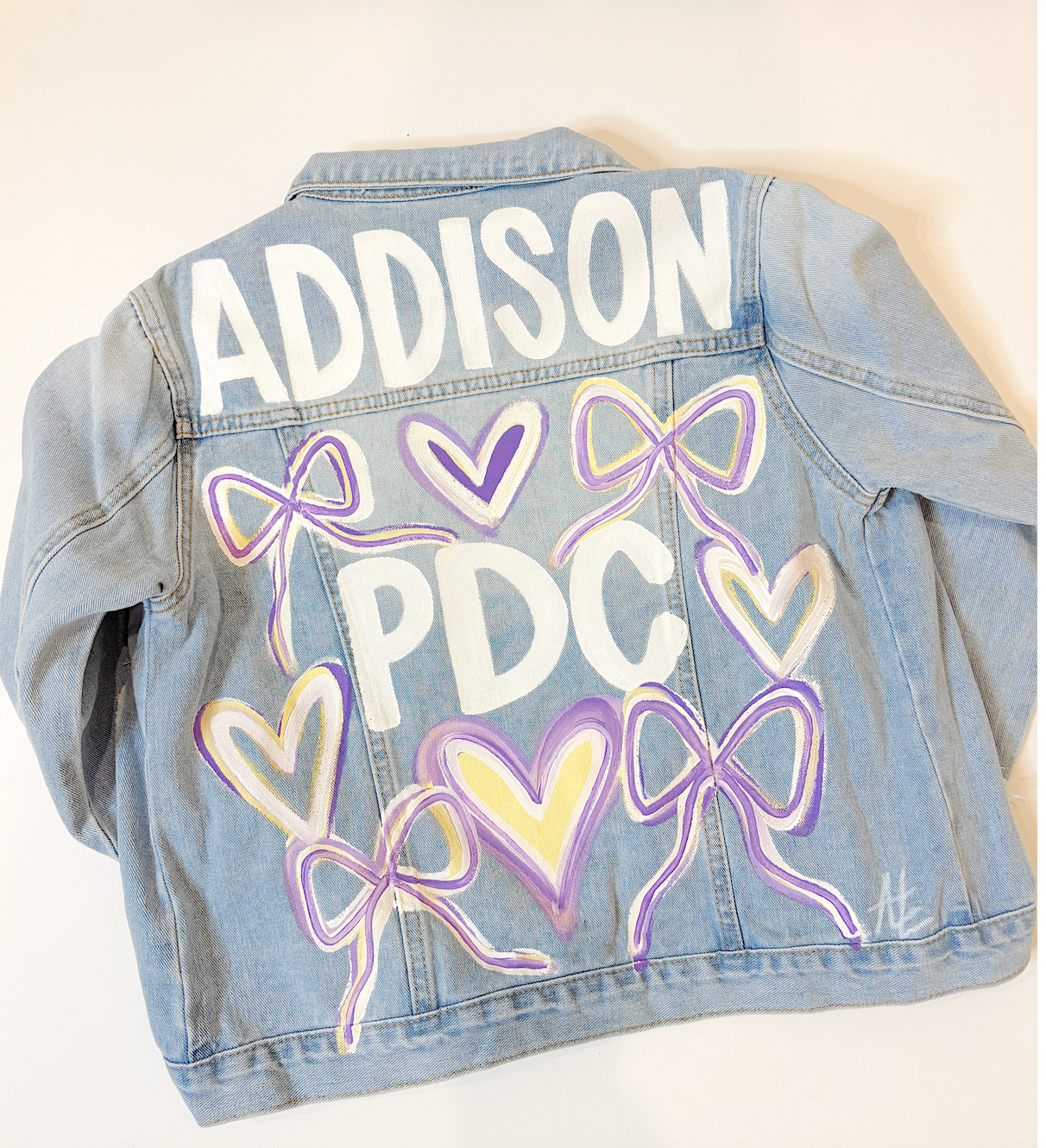 Customized gray denim jacket with white, purple, and yellow painted hearts, the name 'JOSIE' in large white letters on the back, the number '24' in purple, and the word 'Senior' in yellow.
