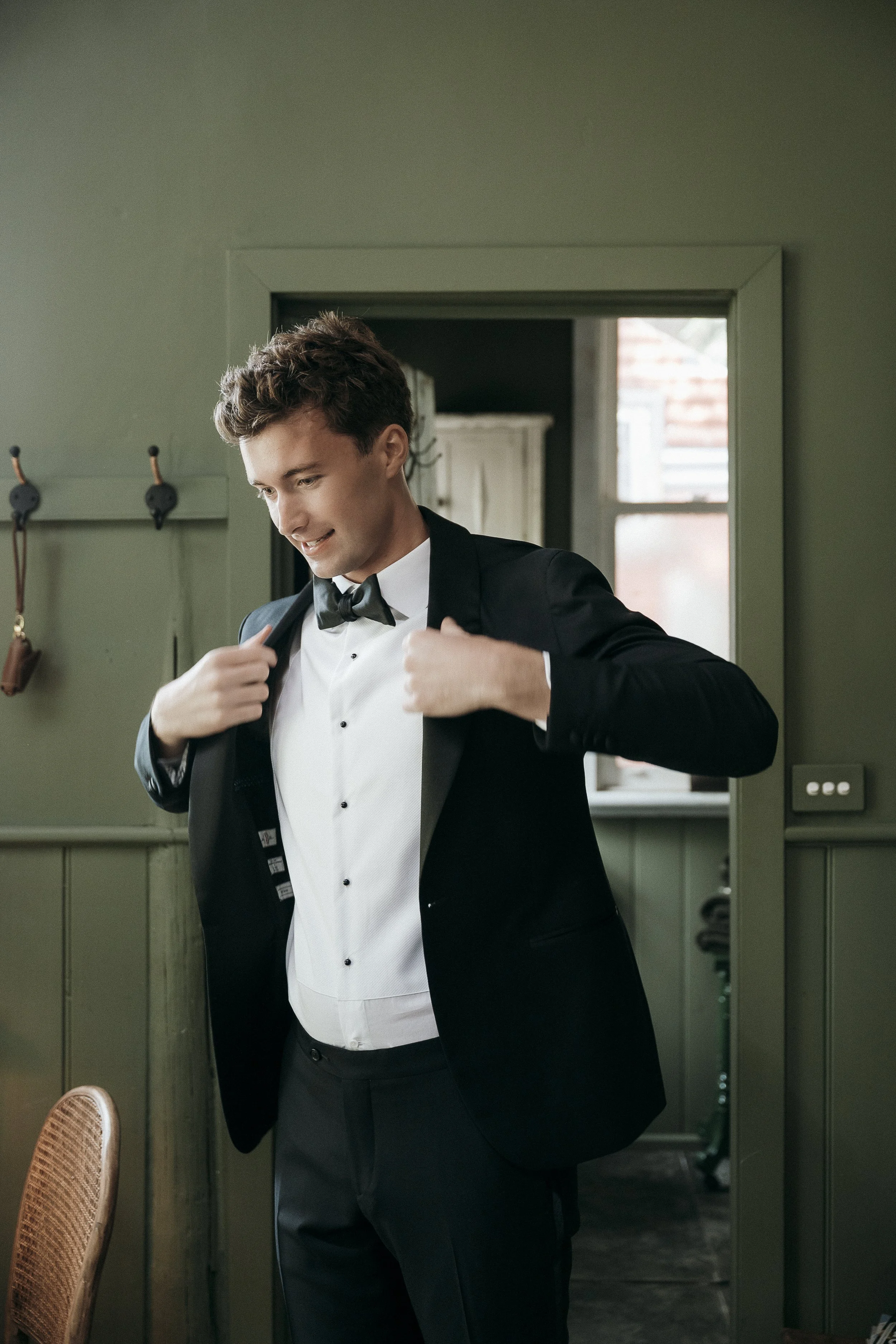 Groom getting ready in the Potting Shed at Acre of Roses, adjusting his tux jacket.