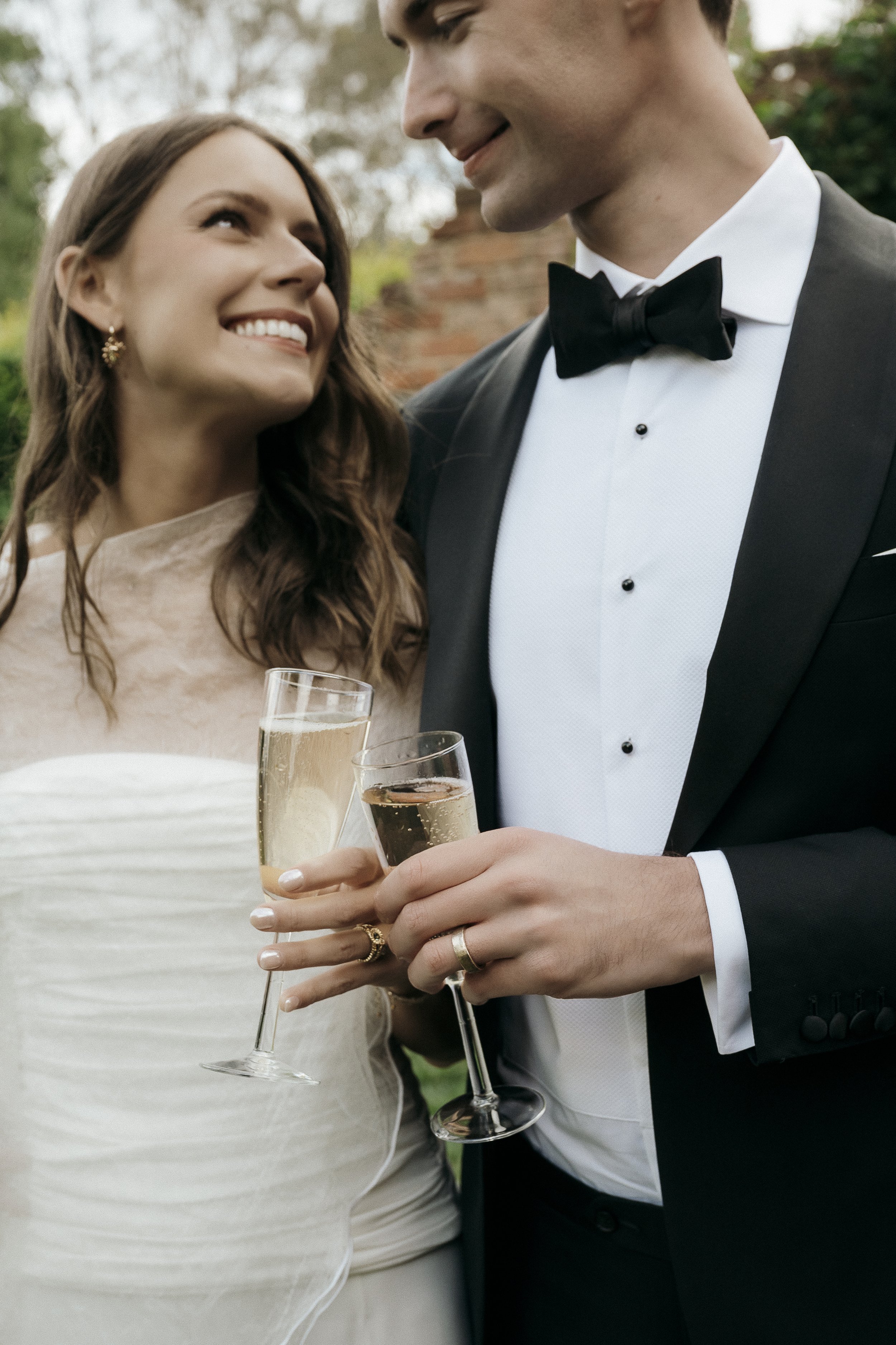 Detail shot of couples rings and champagne glasses as they look at each other laughing and smiling