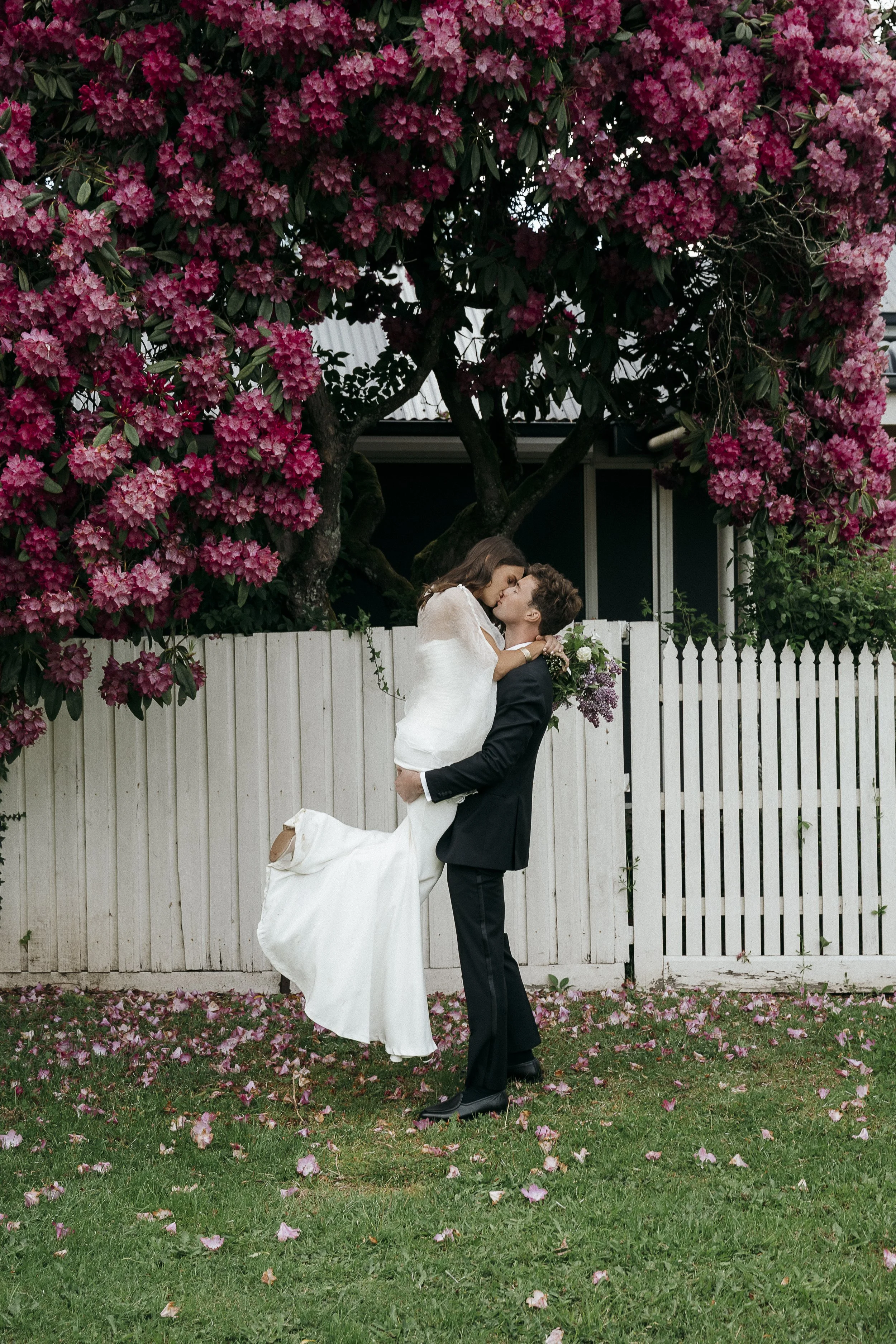 groom sweeps bride off her feet in front of gorgeous purple flowering tree