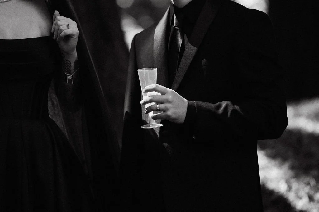  black and white photo of groom holding a glass of champagne in a stream of light his ring being illuminated 