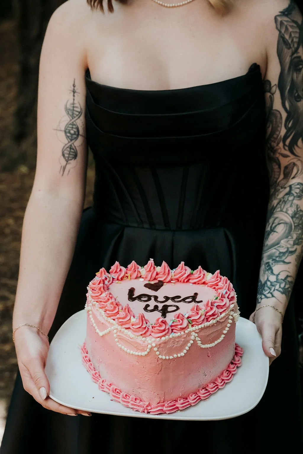  Home made vintage style pink frosted cake with the words Loved Up on top held by bride in black wedding dress 