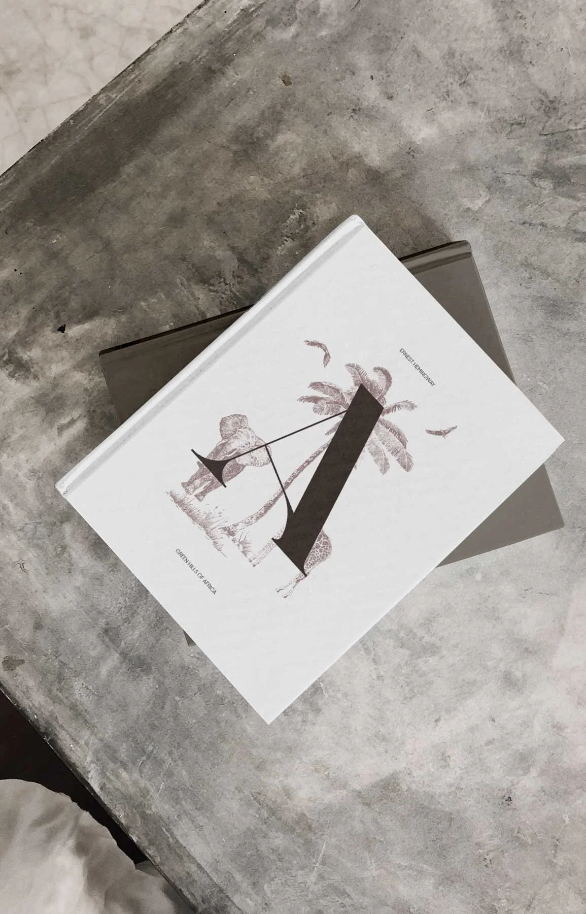 A white book with a design of a lion, a palm tree, and a giraffe on the cover, placed on a gray surface.