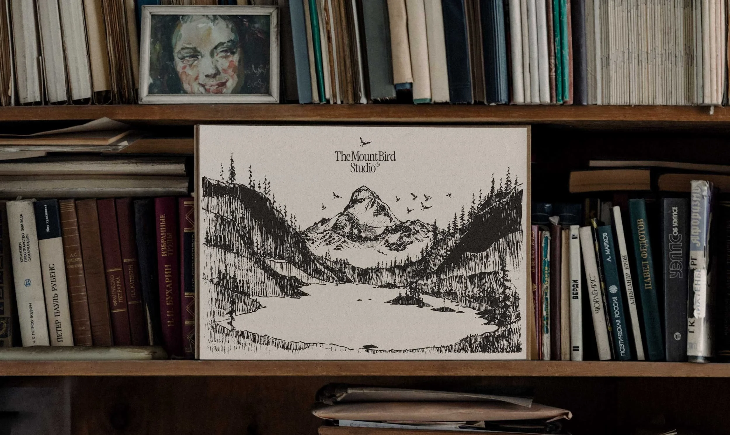 Library shelf with books, there is a sketch of a mountain landscape with trees, a river, and birds flying in front.