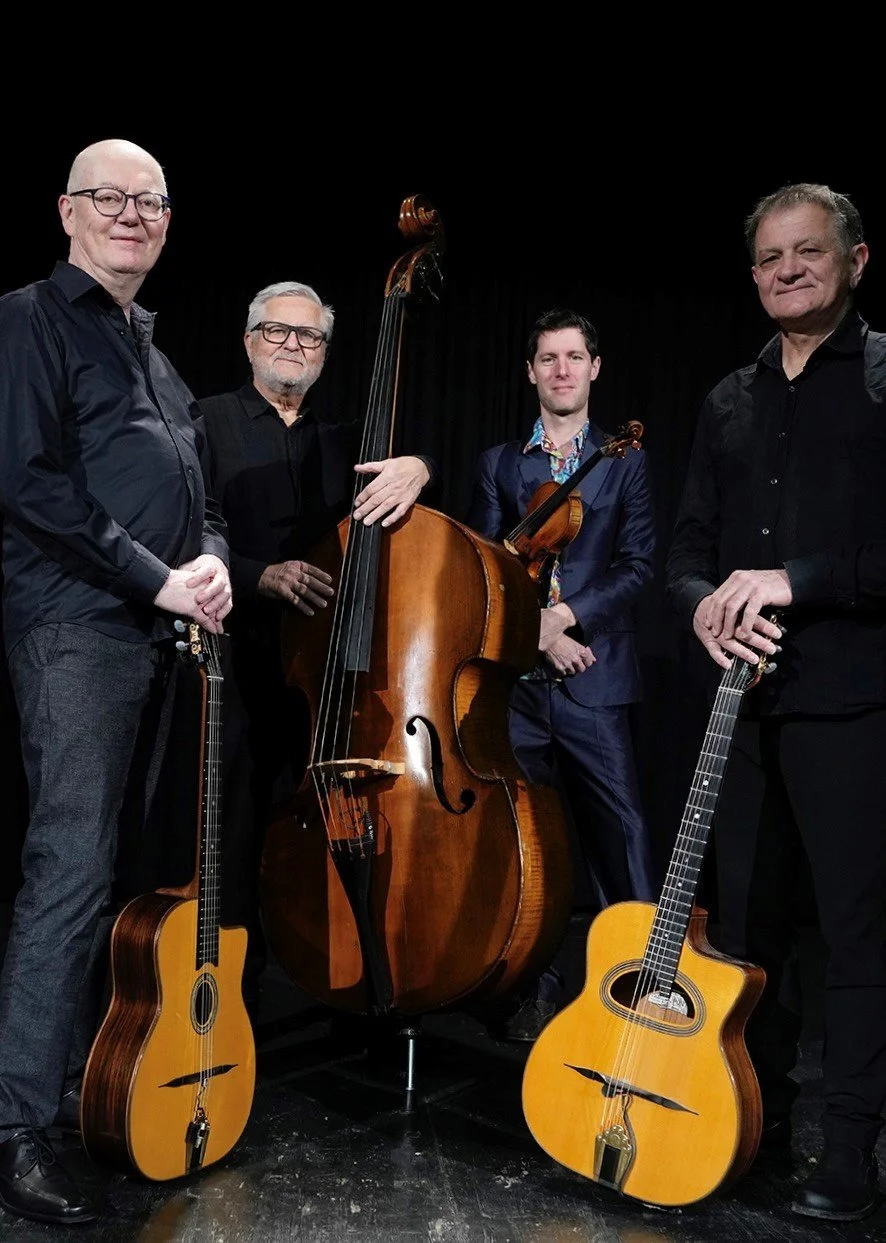4 Herren stehend mit Gitarren und Cello vor schwarzem Hintergrund.