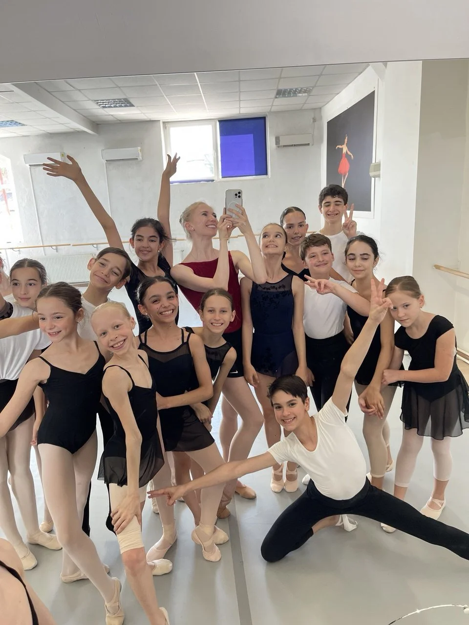Group of young ballet dancers and instructor taking a mirror selfie in a dance studio.