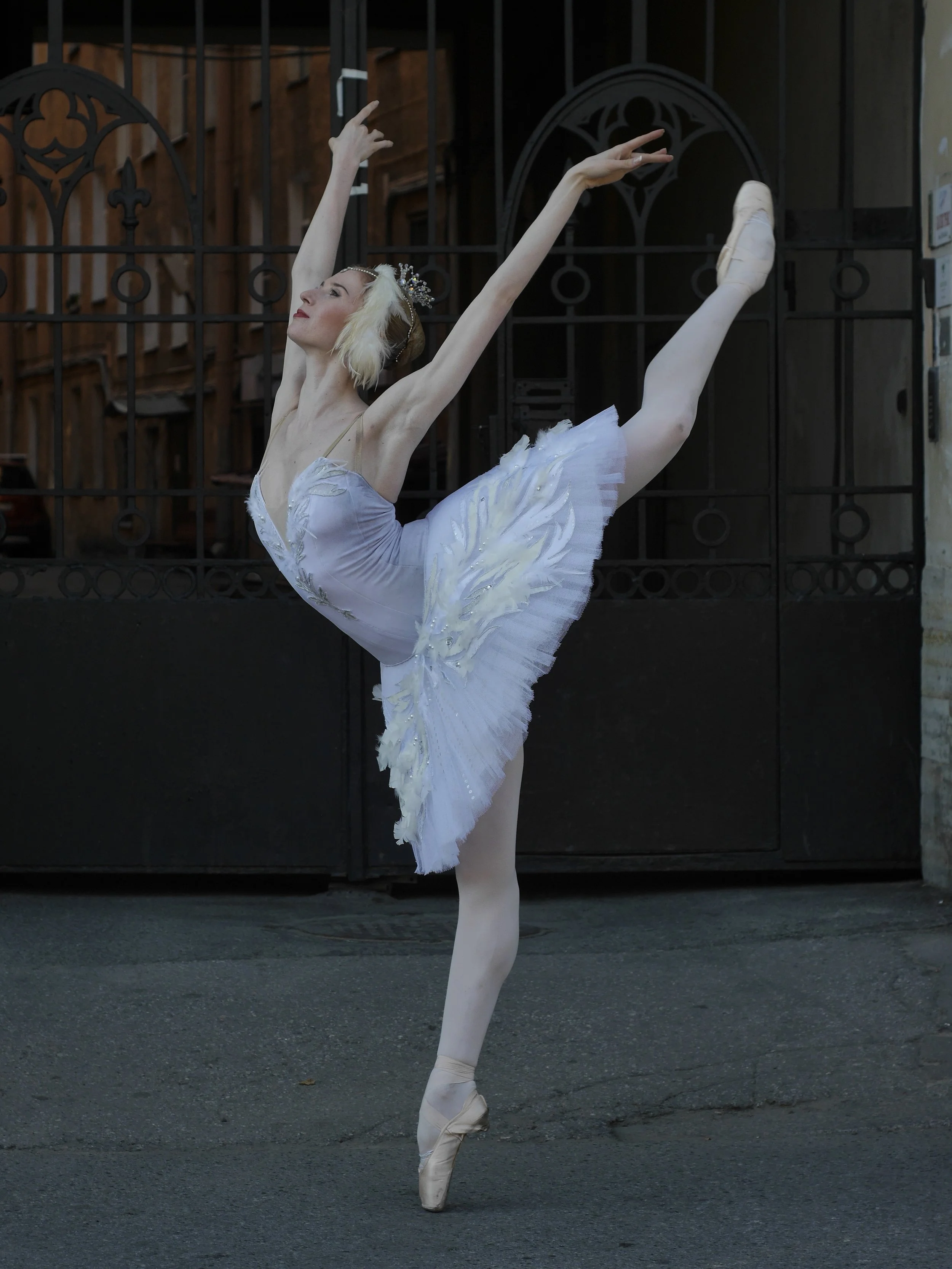 Ballet dancer in a white tutu and pointe shoes performing a ballet pose outdoors.