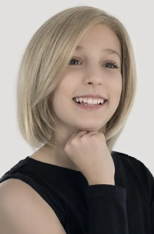 A young girl with blonde hair, smiling and resting her chin on her hand, wearing a black sleeveless top.