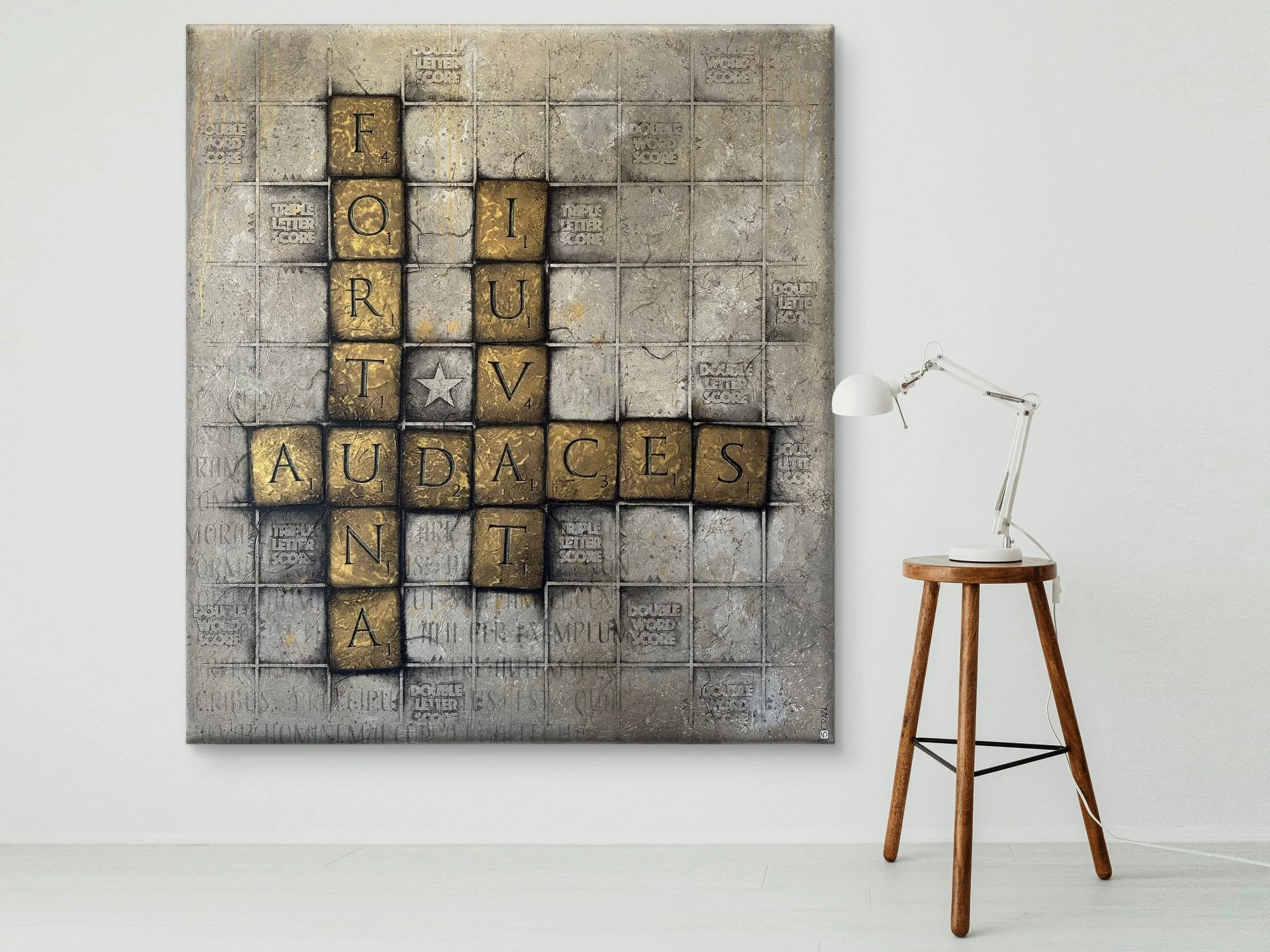 A wall art piece with scrabble tiles displaying the words "FOR" and "TRUST" at the top and "AUDACIOUSNESS" vertically, set against a grey textured background, next to a minimalist white desk lamp on a wooden tripod side table.