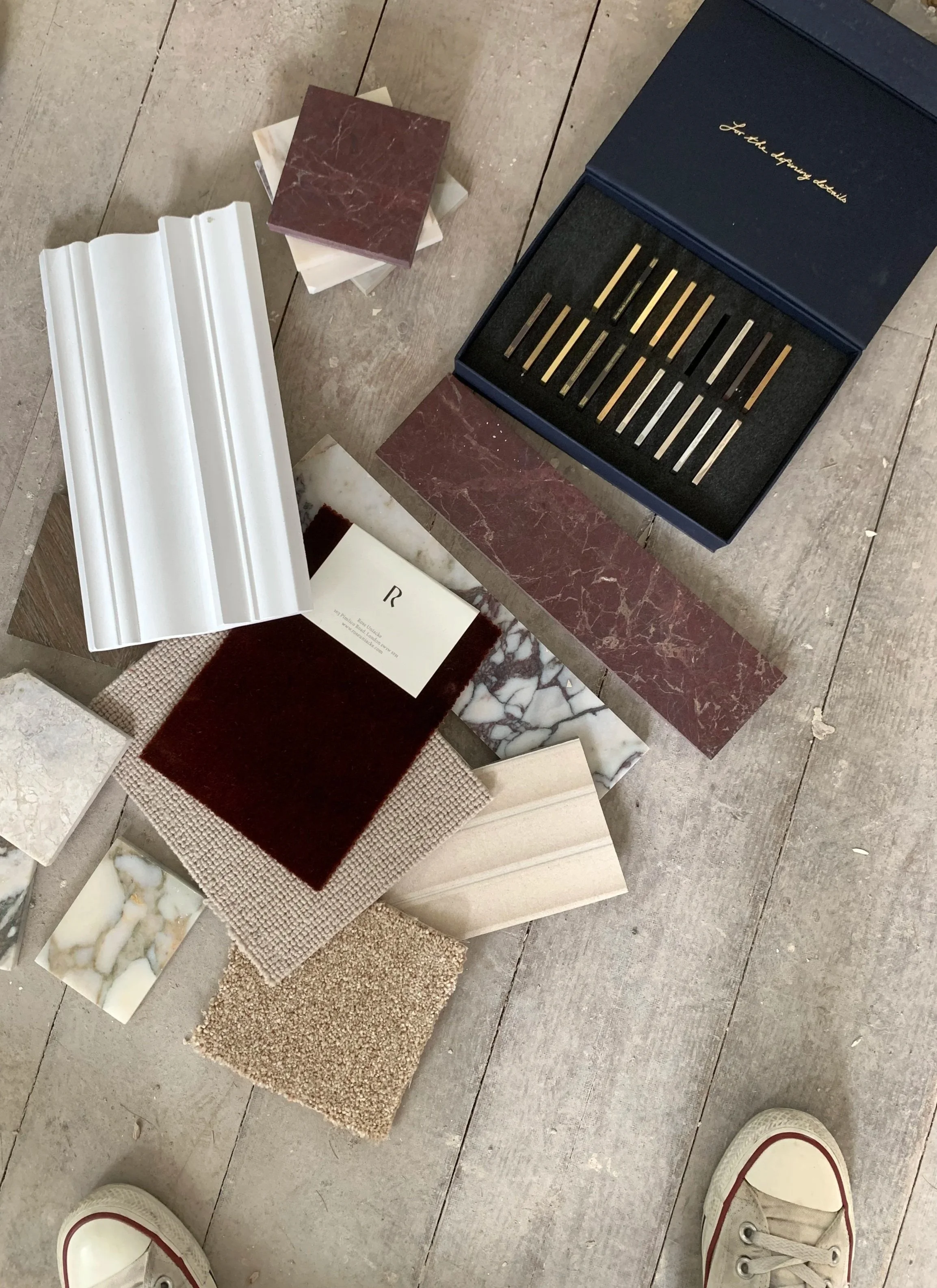 Various samples of decorative material including tiles, fabric swatches, and stone slabs, with a set of precision measuring tools in a box, on a wooden floor.