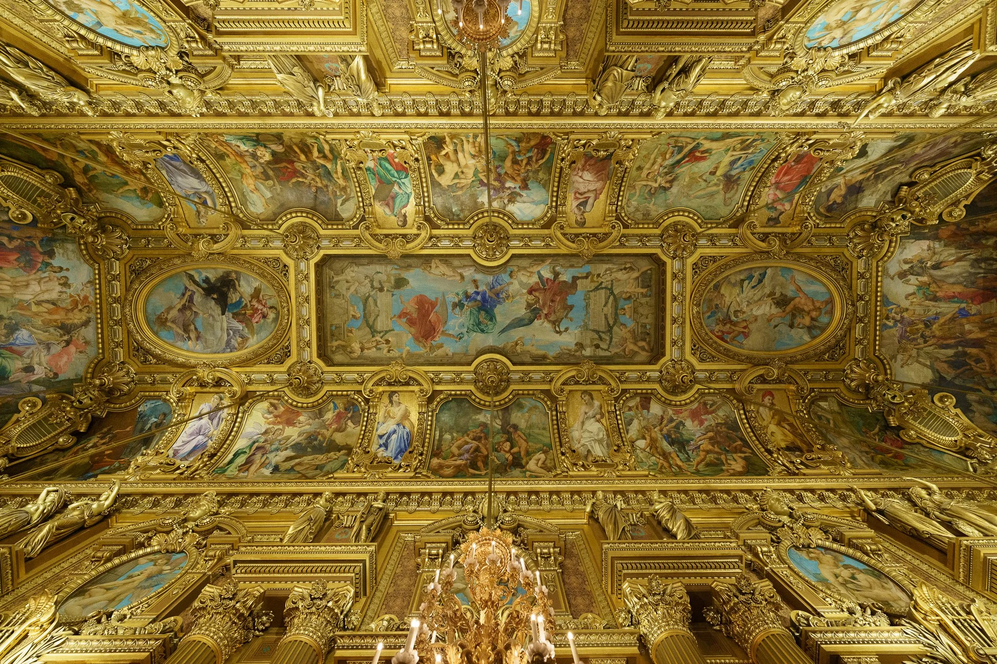 Ornate ceiling with gold detailing and large painted murals depicting mythological scenes in a grand hall.