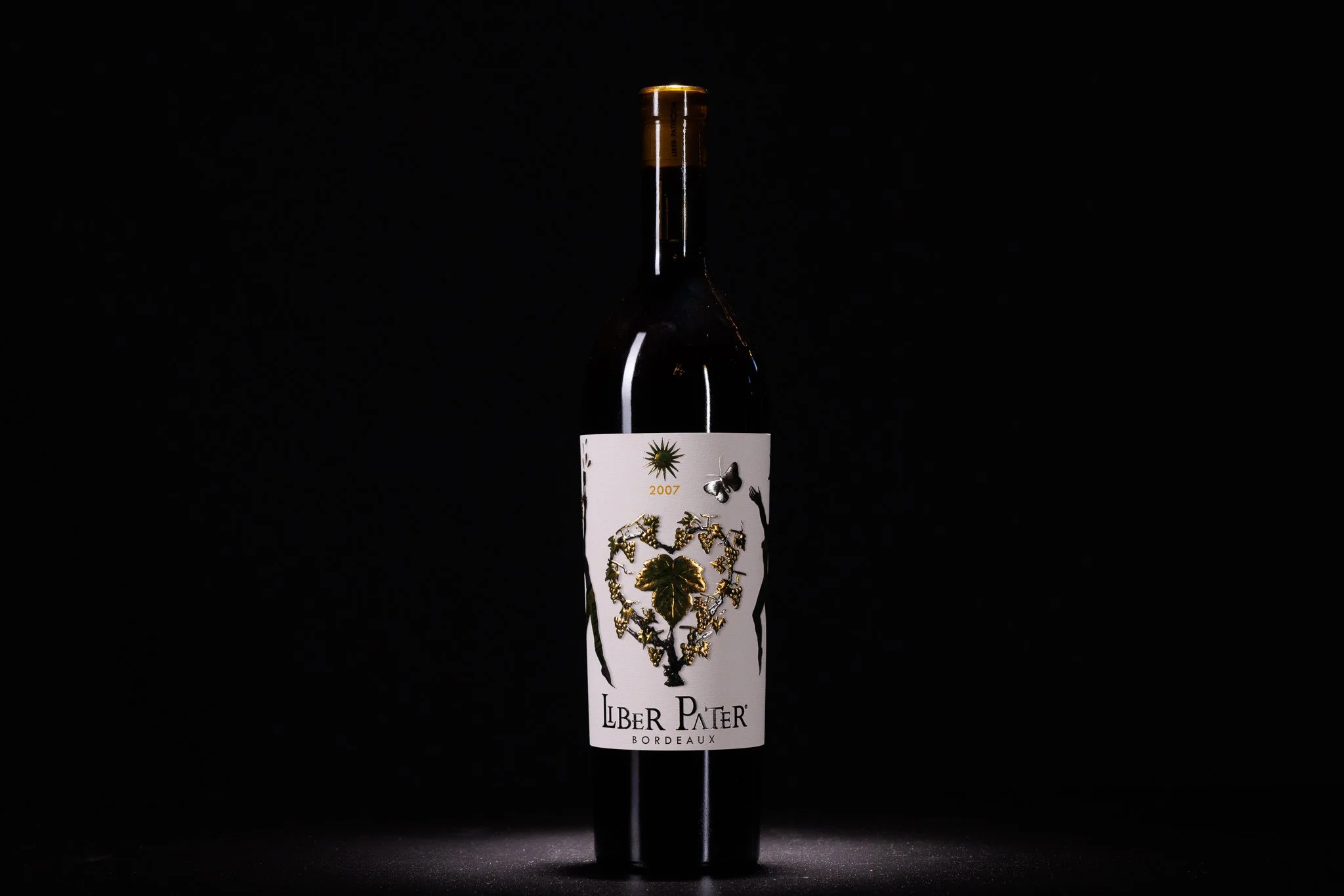 A wine bottle with a white label featuring gold and black leaf designs, set against a dark background.
