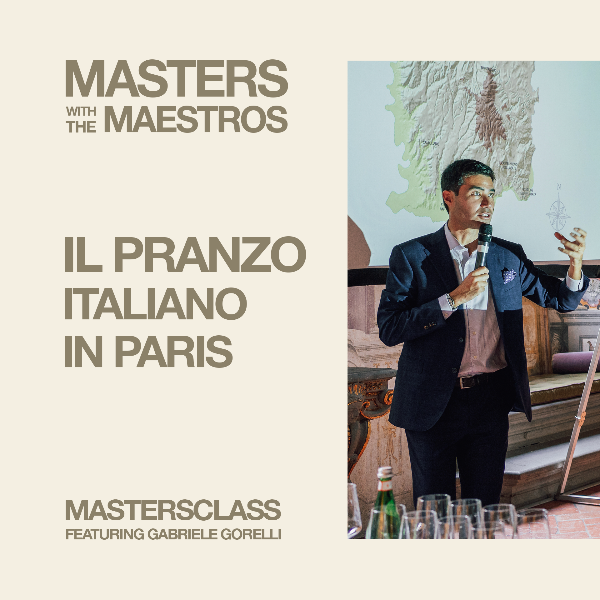 A man in a suit giving a presentation in front of a map of Italy, with glasses and bottles on a table in the foreground.
