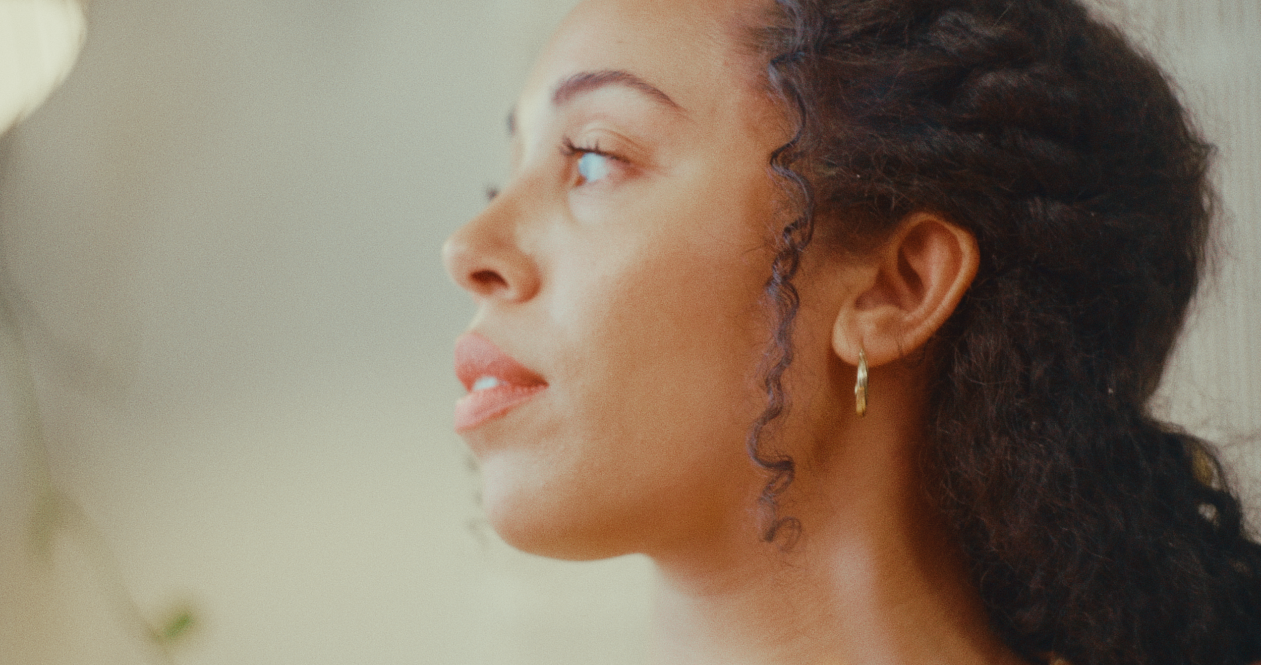 Close-up of a woman with curly hair and earrings looking to the side.