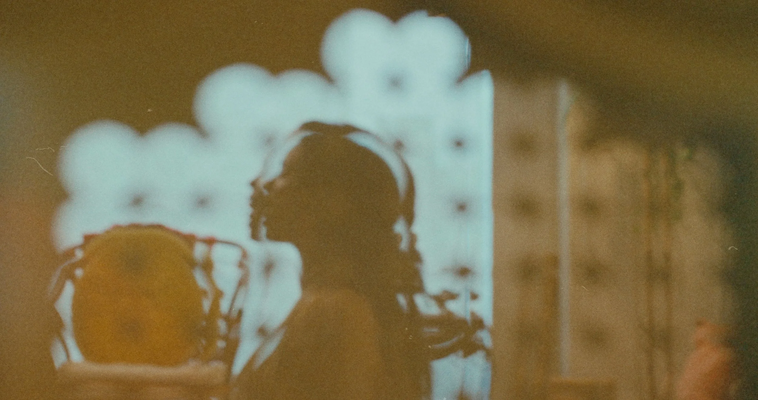 Blurred image of a person taking a reflection selfie in a mirror, with a bright light or illuminated frame in the background.