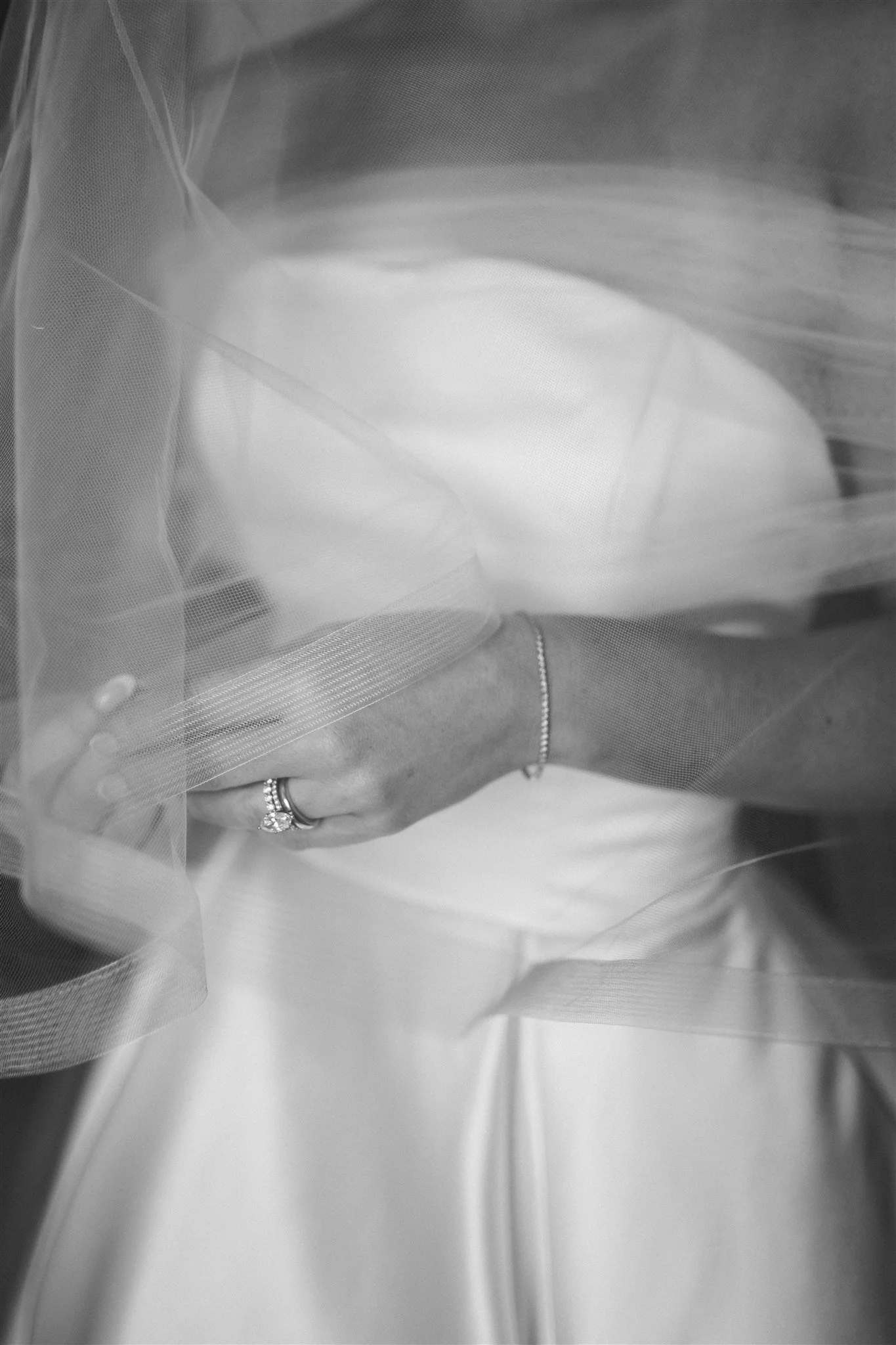 Close-up black and white detail photo of bride's hand with diamond engagement ring holding wedding dress through tulle veil — Lake Tahoe wedding photography by Elsa Boscarello