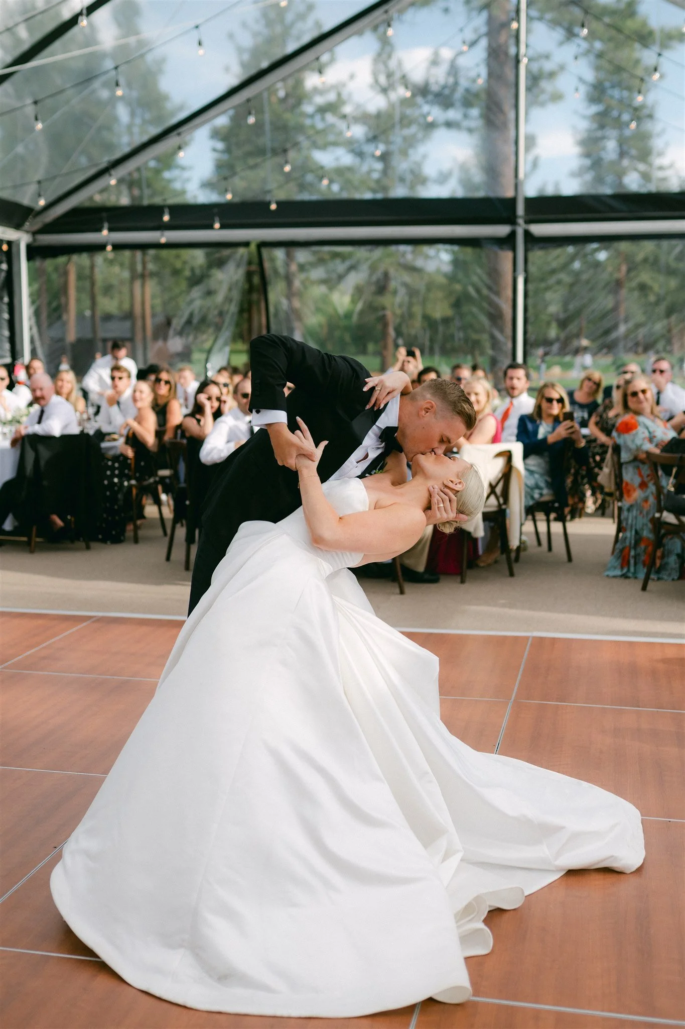 Clear tent wedding reception dinner at Edgewood Tahoe Resort with guests seated at round tables with white linens, greenery centerpieces, and string lights overhead — Lake Tahoe wedding reception