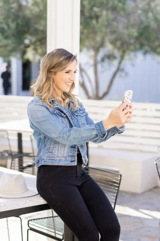 San Diego Social Media Marketing Manager, Kellen Dieterich, sitting outside at a table, taking a selfie with her phone.