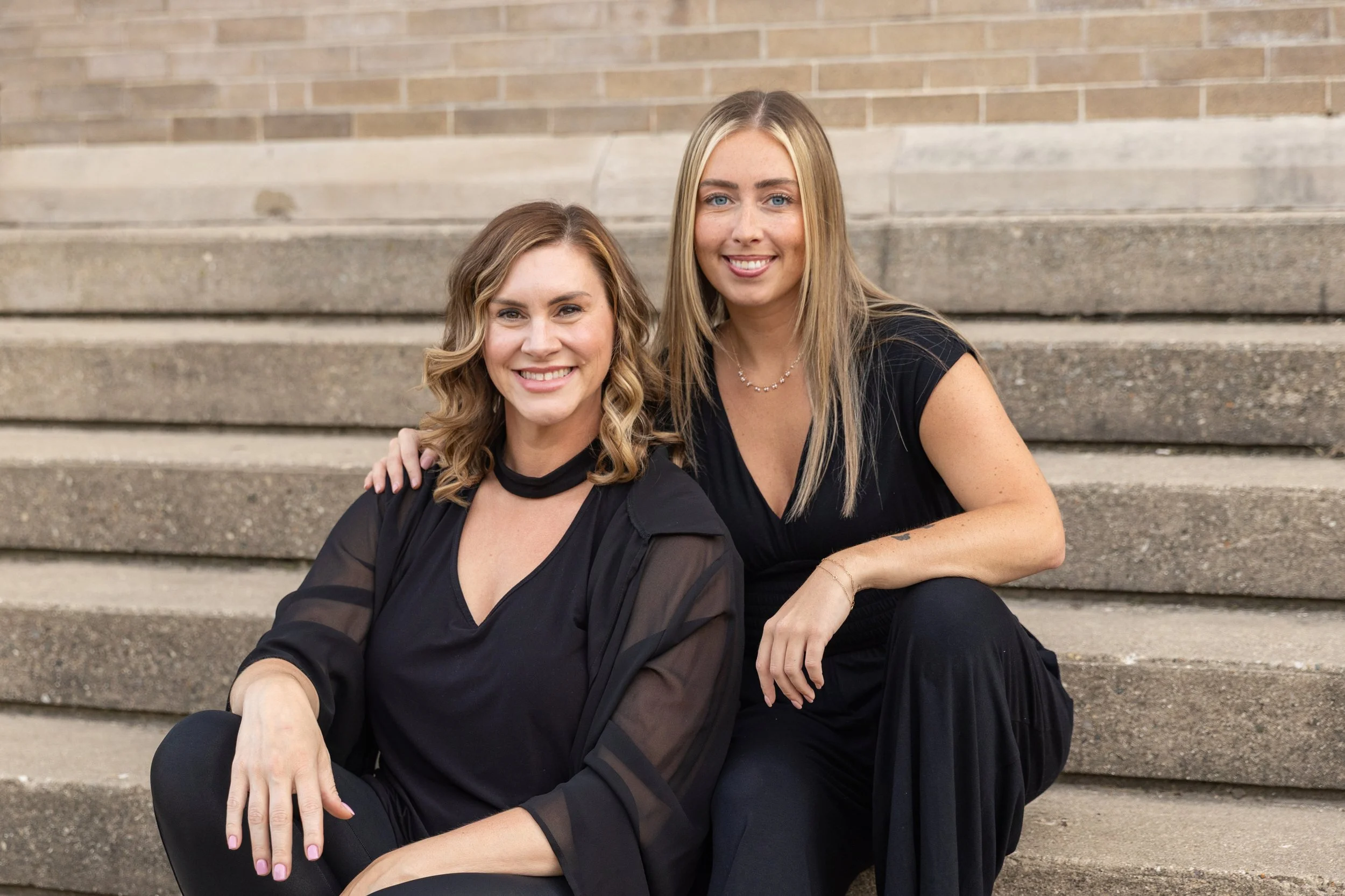 Licensed estheticians Jess and Emily sit on steps in Janesville, WI