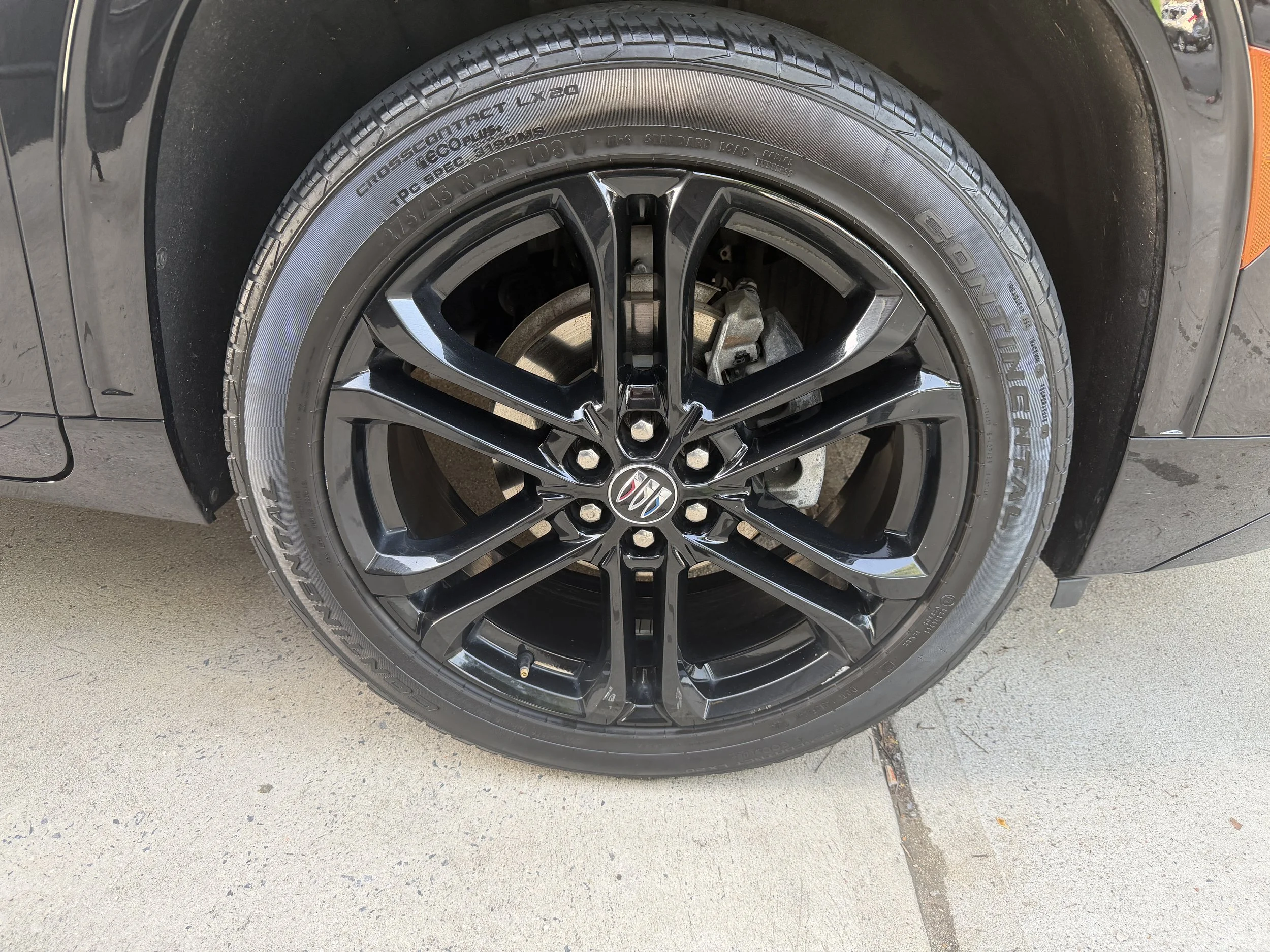 Close-up of a black car wheel with a silver rim and a tire, parked on a concrete surface.