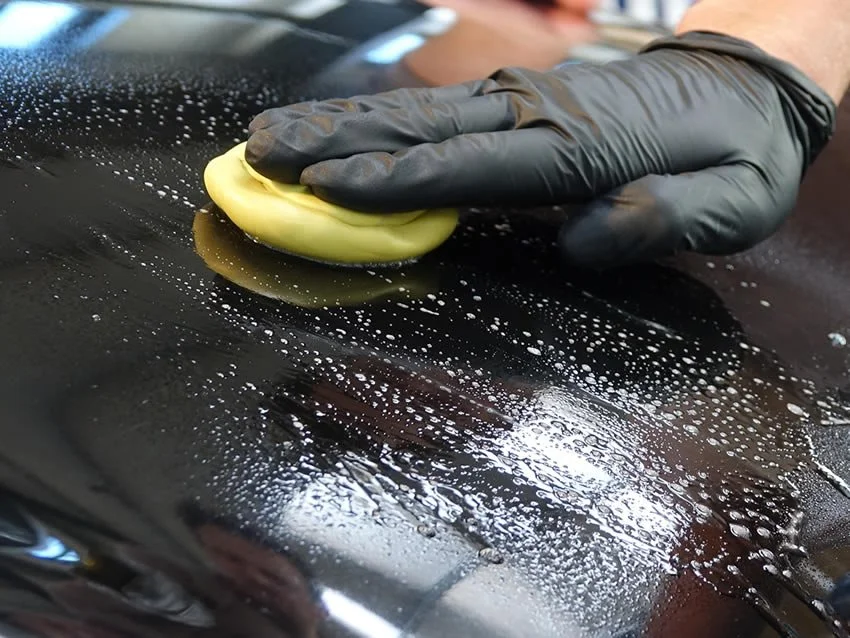 Clay bar being worked across wet dark paint panel with lubricant
