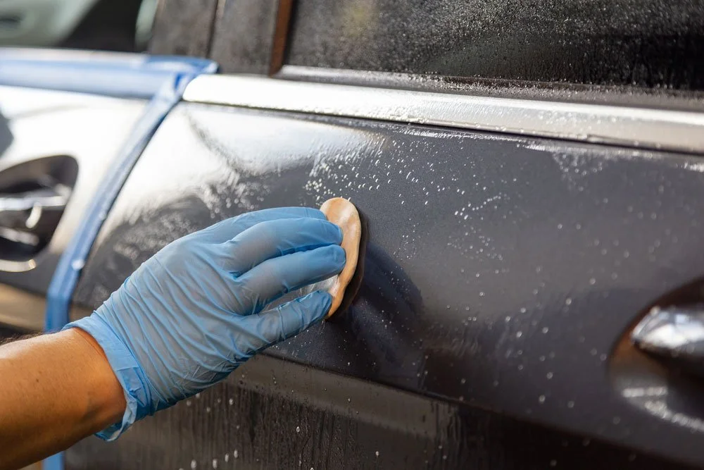 Gloved hand working clay bar across wet paint panel during decontamination
