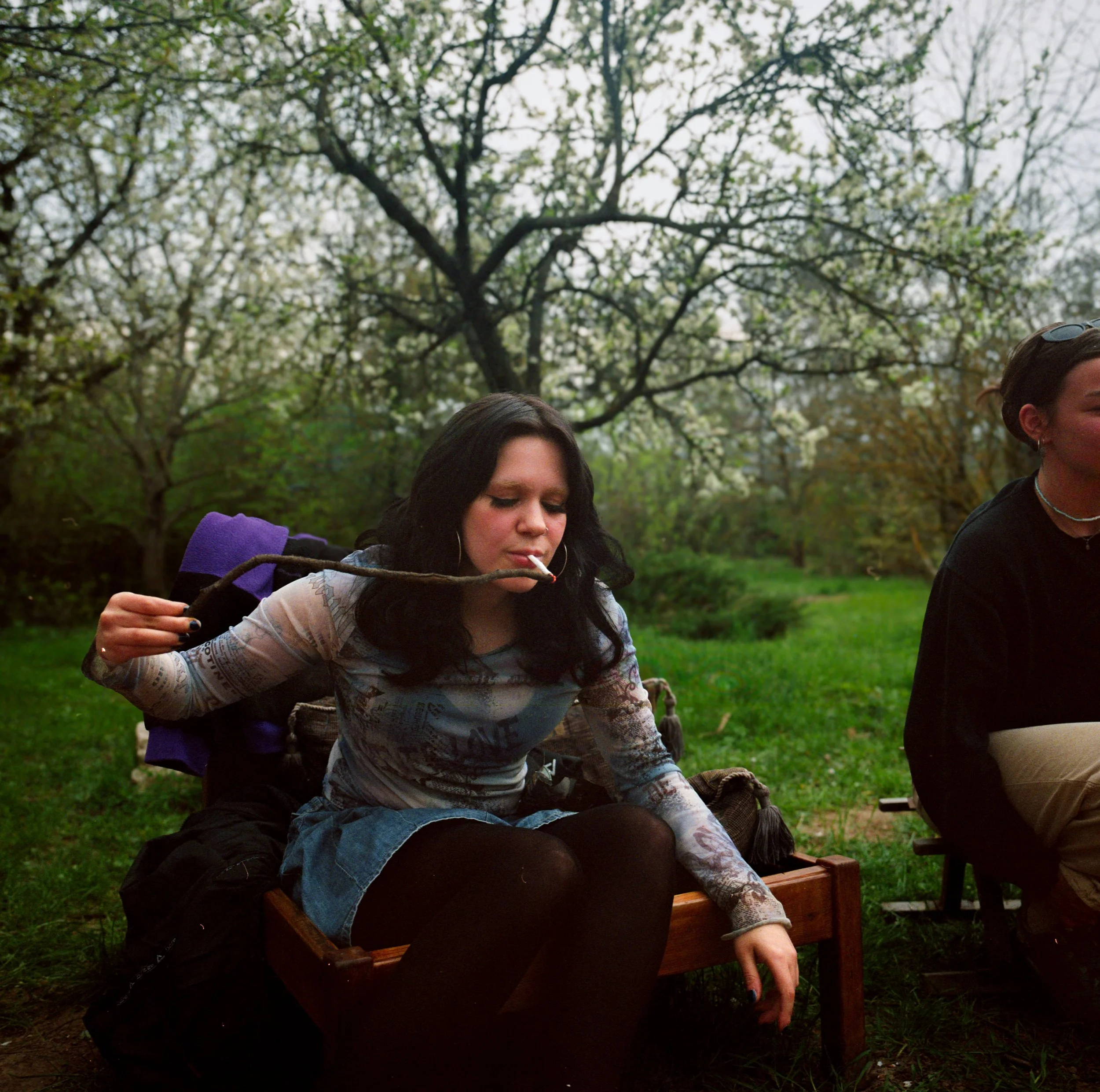 Young person lighting a cigarette in a garden with a tree branch