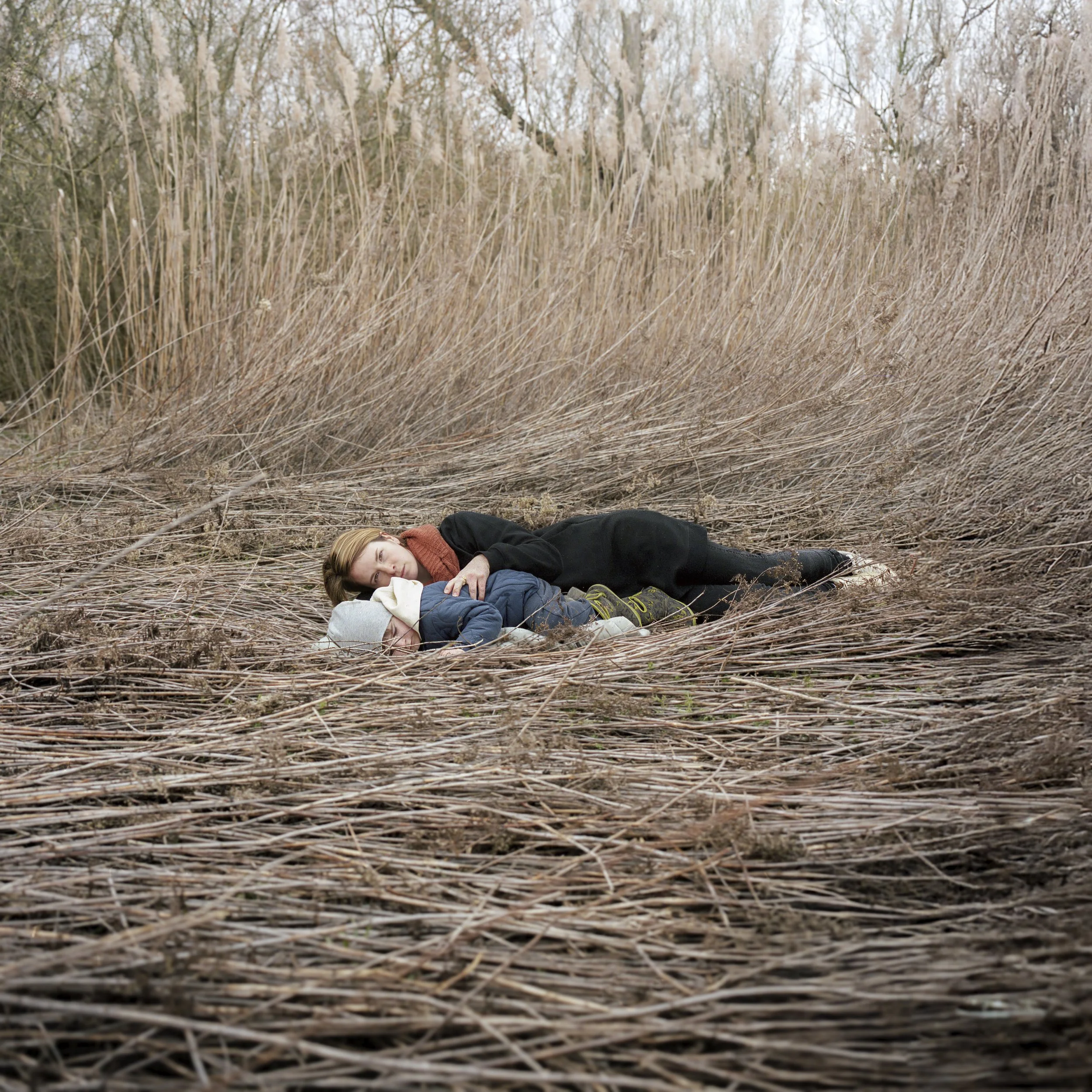 Two people lying in tall reeds near riverbank