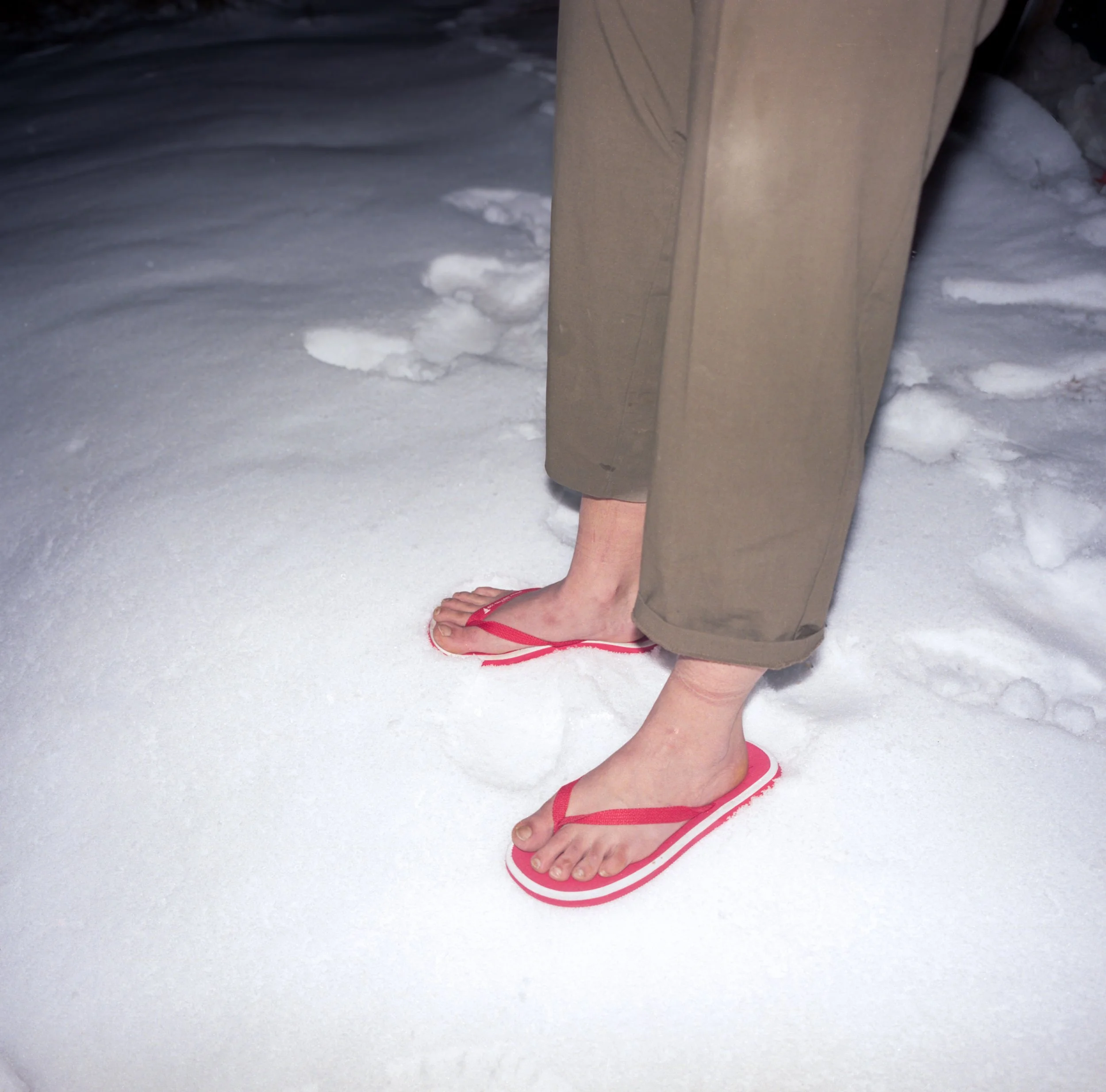 Feet standing barefoot in snow wearing sandals