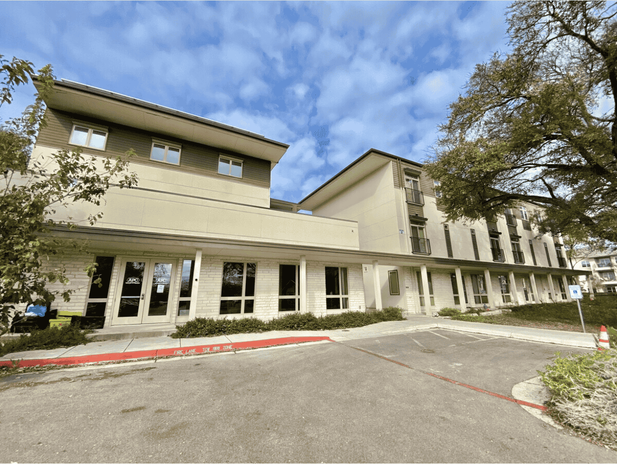 Two beige buildings pictured from a parking lot.