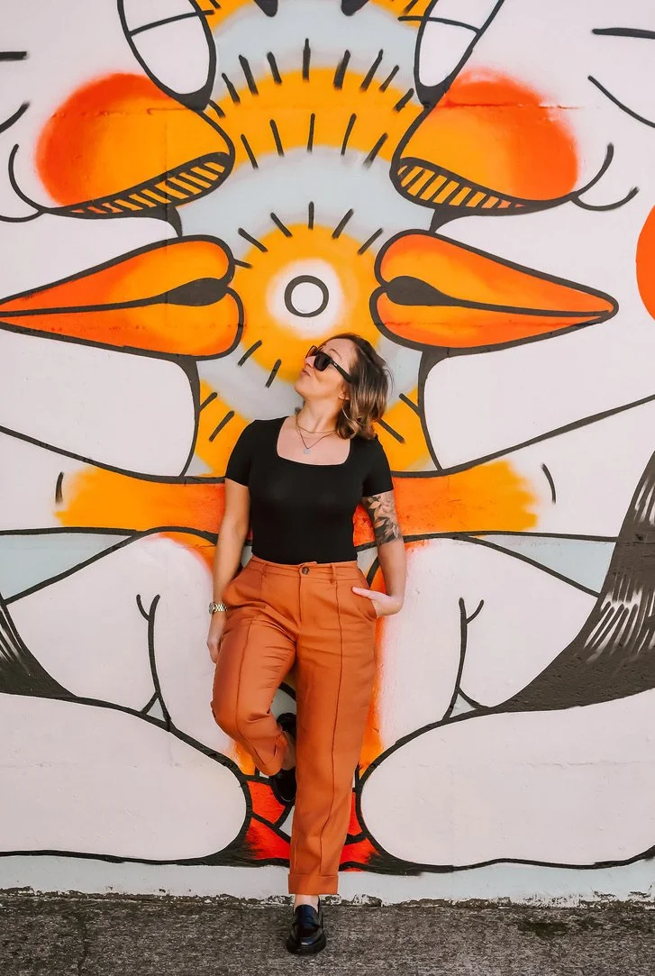 Woman standing against a colorful graffiti mural of a stylized lion's face.