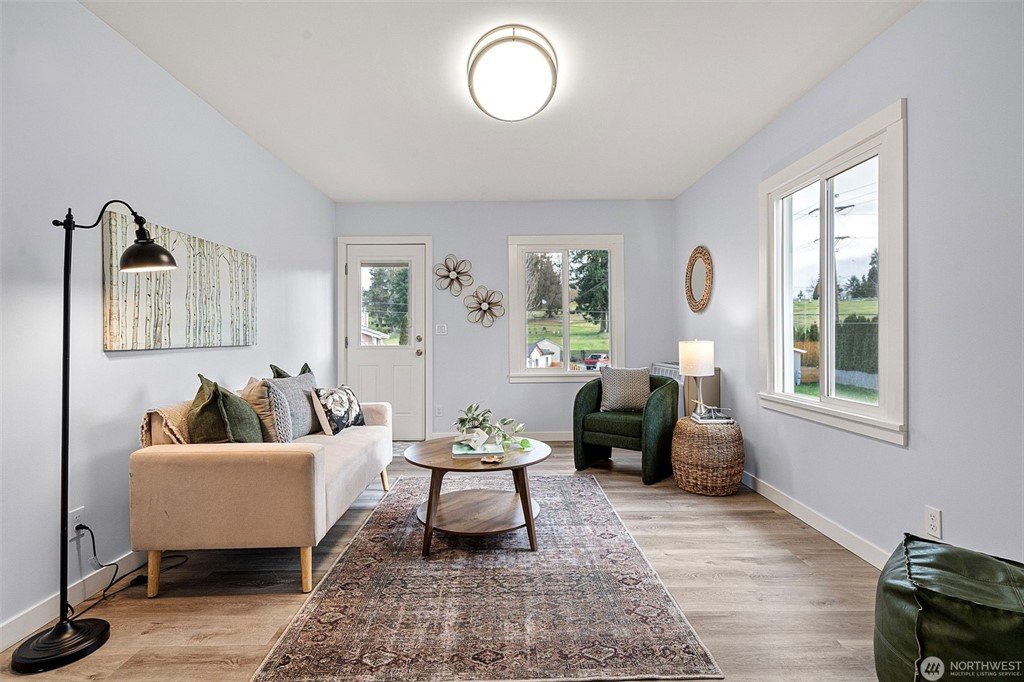 Living room with a beige sofa, green armchair, side table with lamp, window view of yard, and decorative wall art.