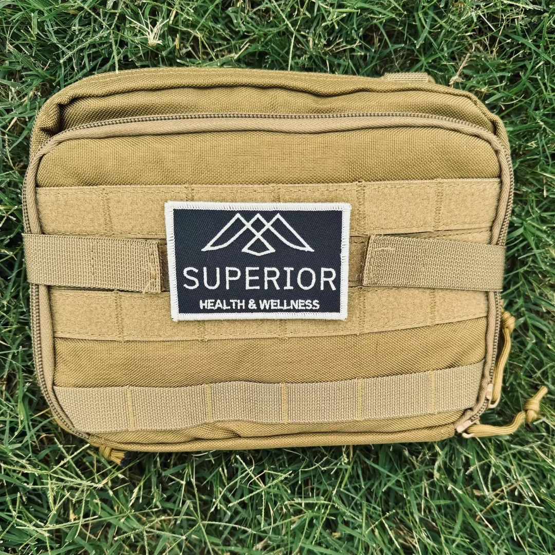 Tan tactical bag on grass with a patch that reads 'Superior Health & Wellness' with geometric mountain design.