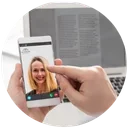 Person taking a selfie with a smartphone, newspaper in the background