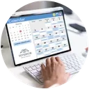 Person using a tablet with a calendar app open, on a desk with a keyboard, mouse, and pen