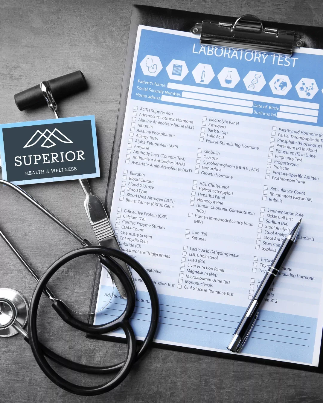 A medical clipboard holds a laboratory test form, with a stethoscope, a pen, and a small black flashlight nearby, and a health and wellness card on the side.