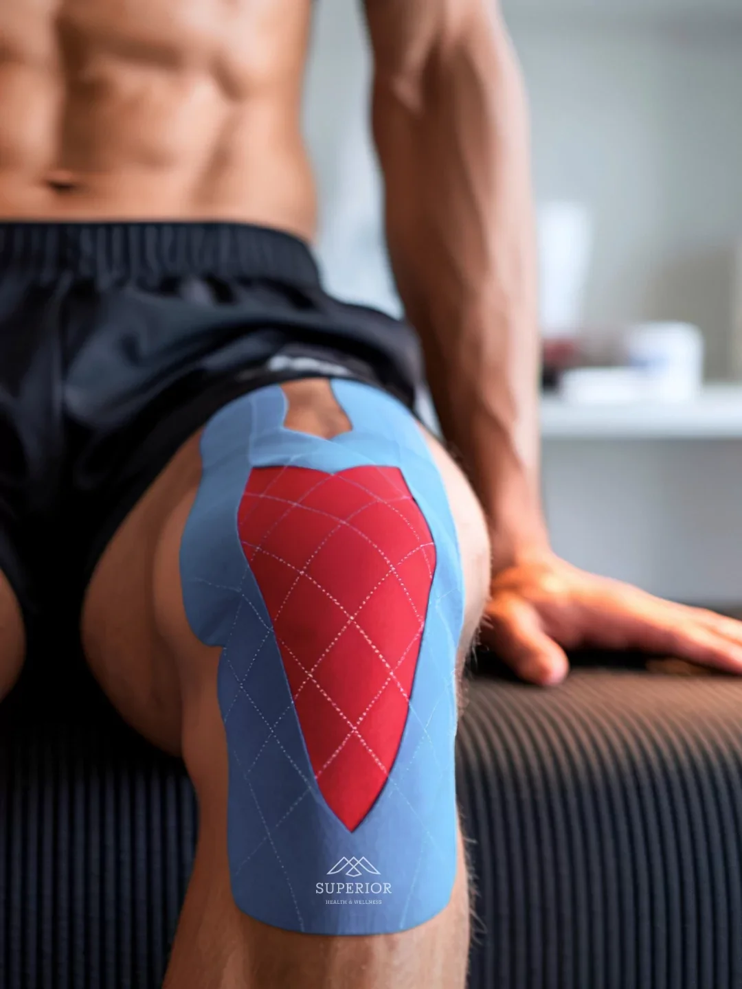 A person with a muscular body sitting on a surface, with kinesiology tape on their thigh, marked with a red target pattern and the words "Superior Health & Wellness"