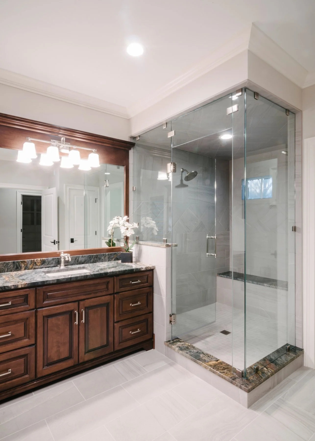 Custom walk-in shower with glass doors next to dark wood vanity