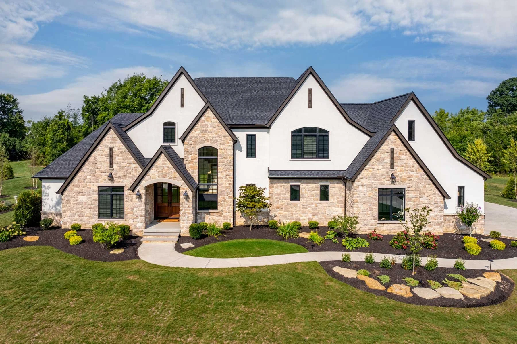 Custom luxury home exterior with white stucco, stone accents, dramatic gabled rooflines, and landscaped front yard.
