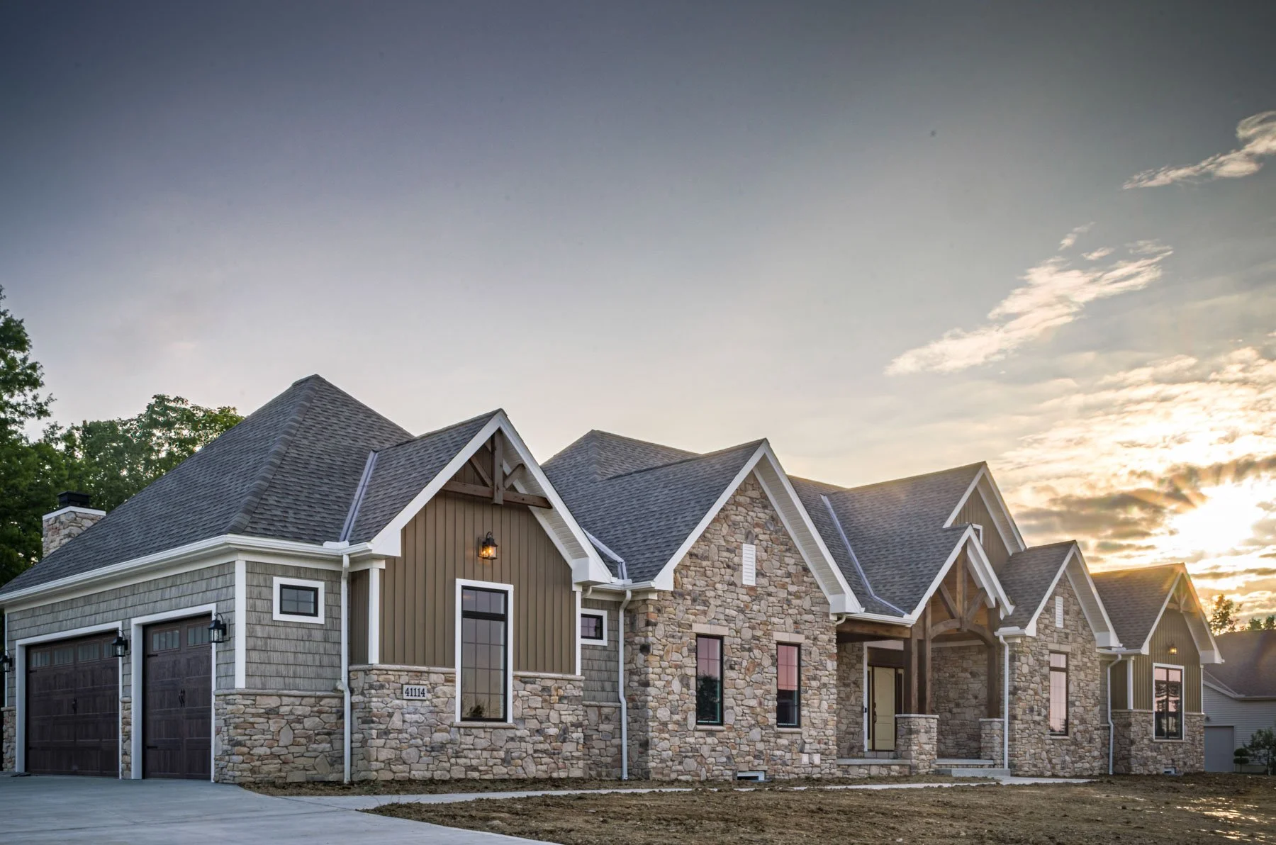 Custom stone exterior home with multiple gabled rooflines, dark garage doors, and rustic architectural accents.