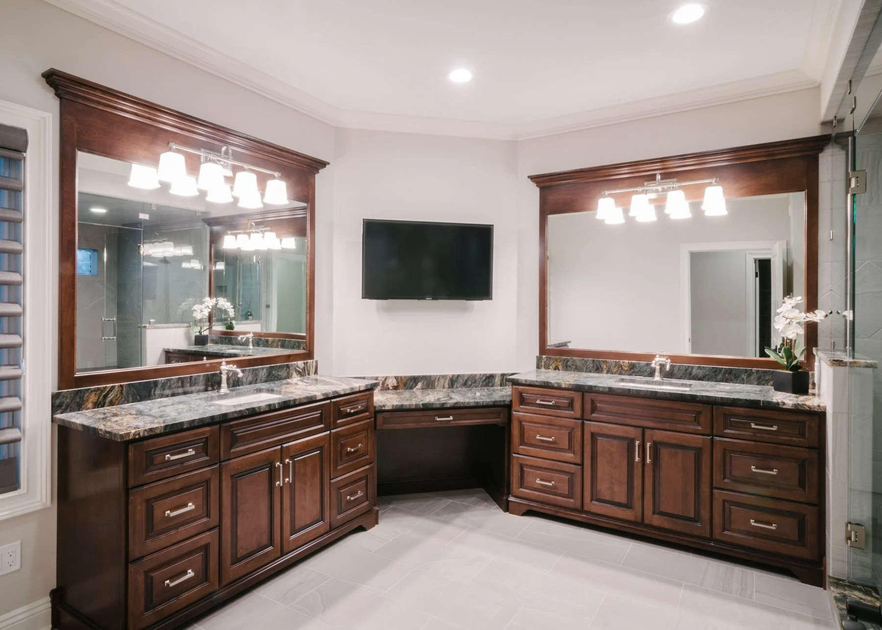 Custom luxury bathroom with symmetrical vanities in dark wood and TV in  corner between them
