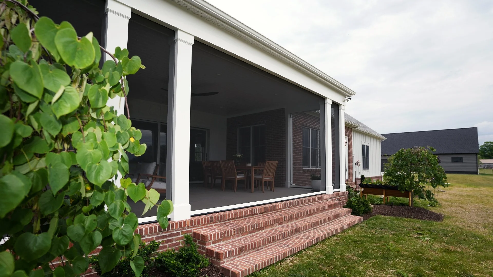 Custom screened porch with white columns, brick foundation, and outdoor seating area behind a modern farmhouse-style home.