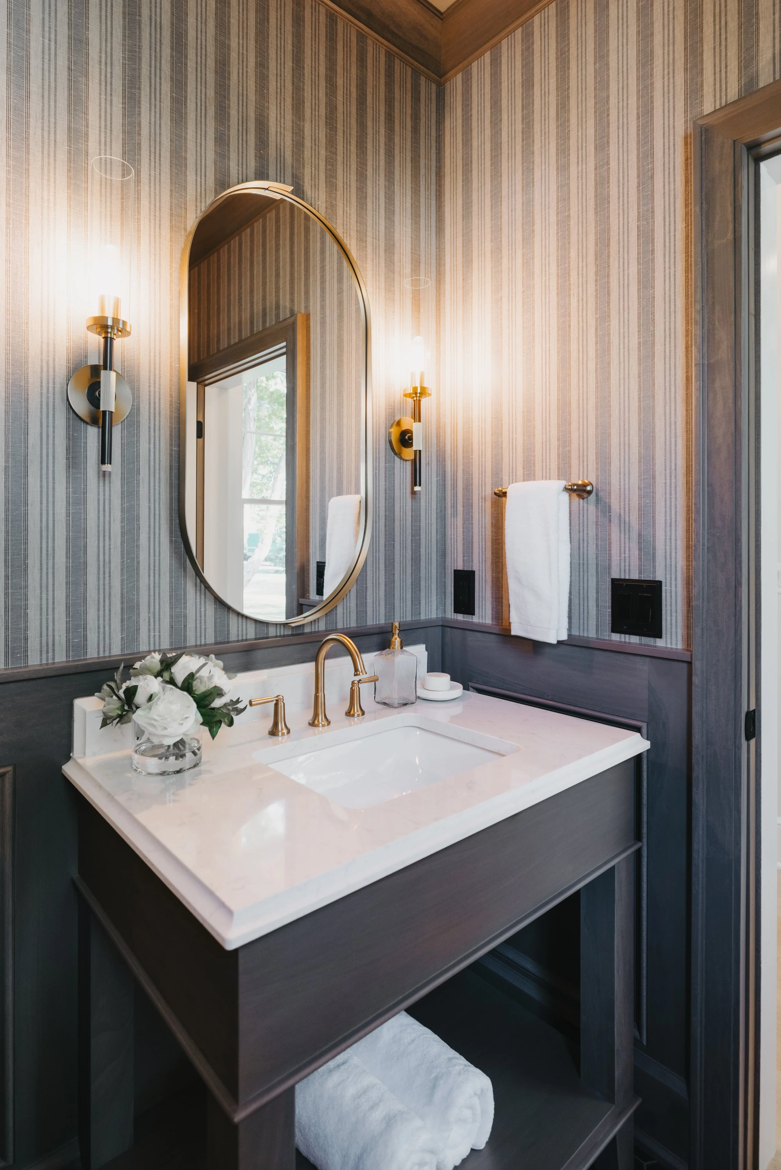 Bathroom sink with striped wallpaper, dark wood vanity, white countertop, and gold fixtures