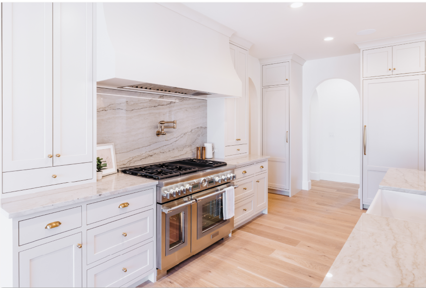Bright white kitchen with marble backsplash, large range, and brass hardware
